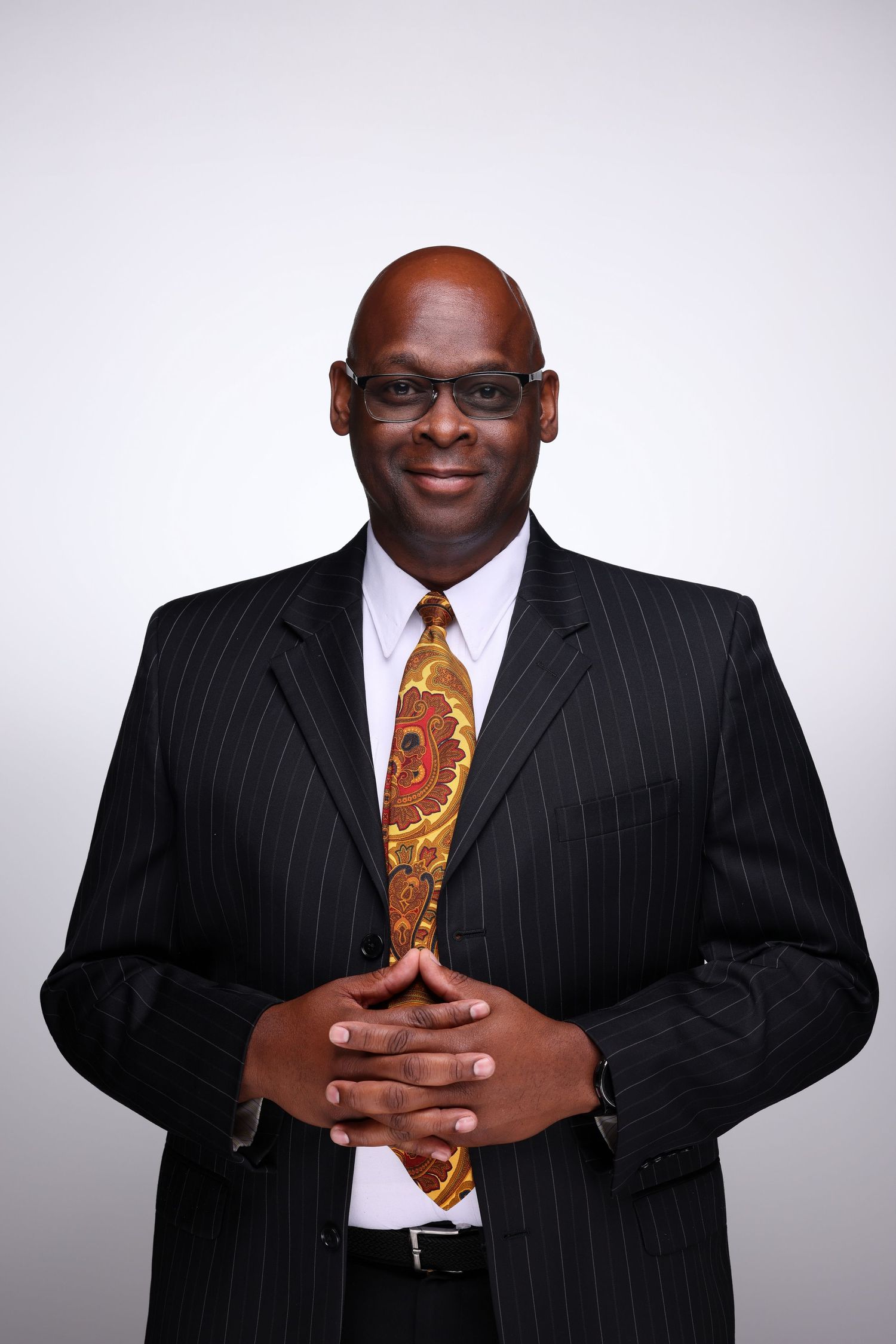 Bald businessman in pinstripe suit with colorful paisley tie smiling confidently.