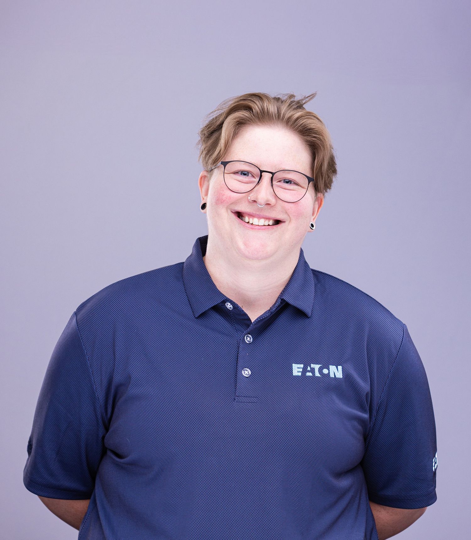 Professional portrait of person in navy Eaton polo with glasses against purple background.