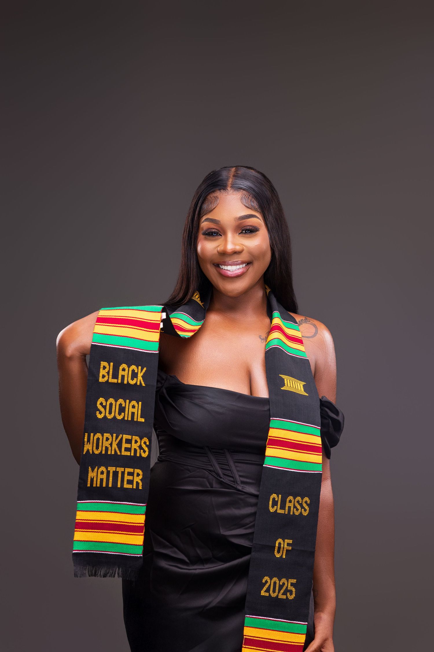 Graduate wearing black dress and cultural graduation stole with colorful striped pattern.