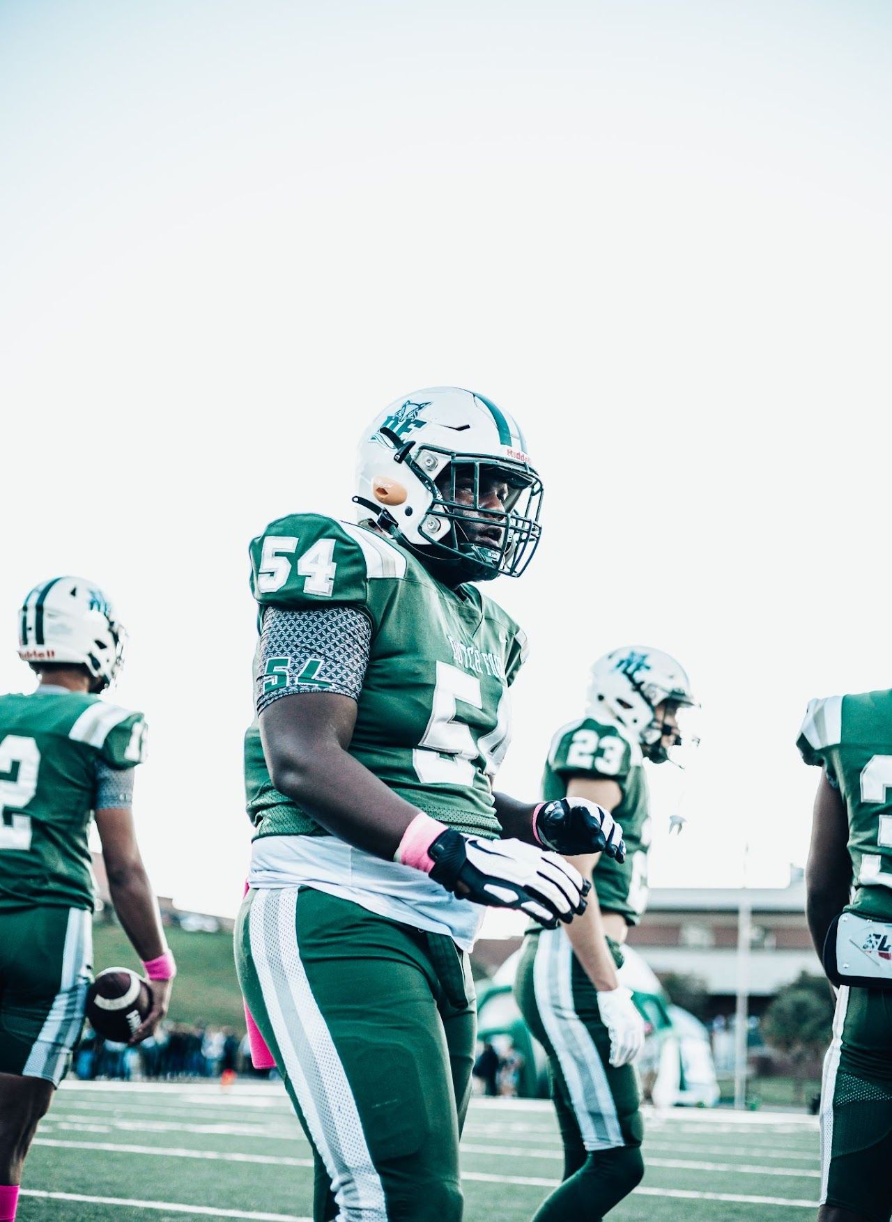 Football player in green and white jersey stands on field during practice or game.  DFHS
