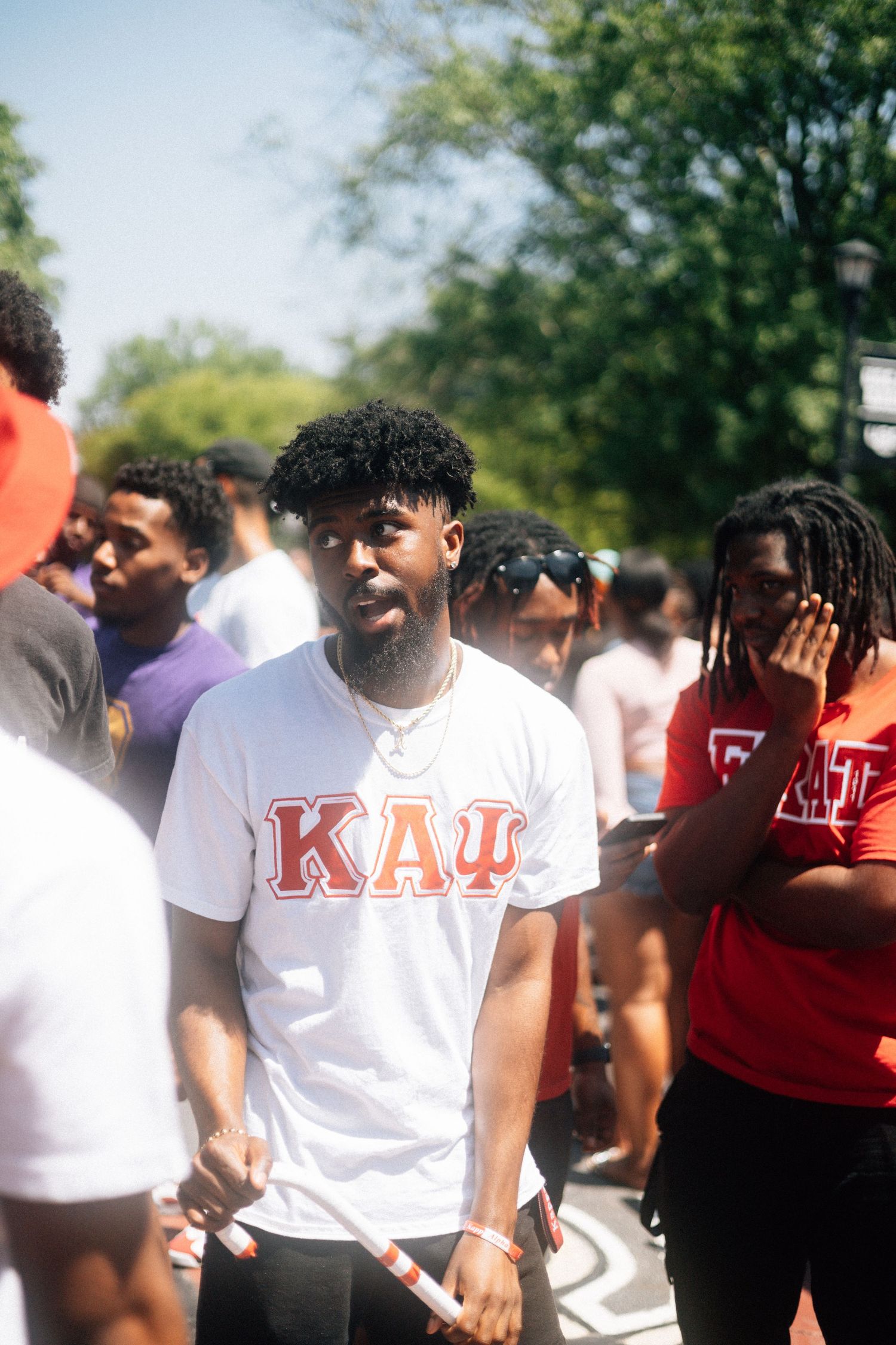 Group of students in white and red shirts gather outdoors during a sunny day.