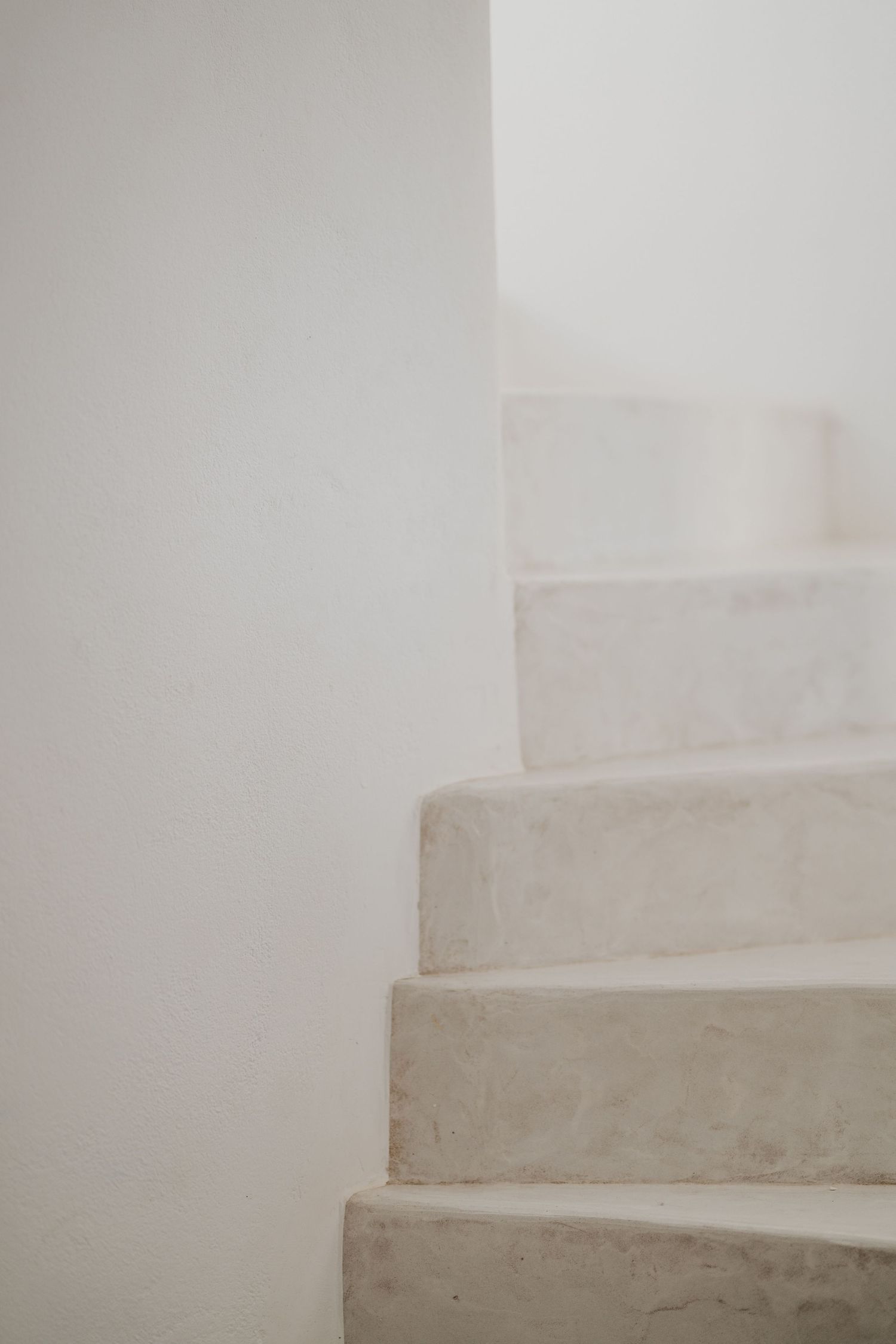 Minimalist white concrete staircase with soft curves and shadows against a plain wall interior.