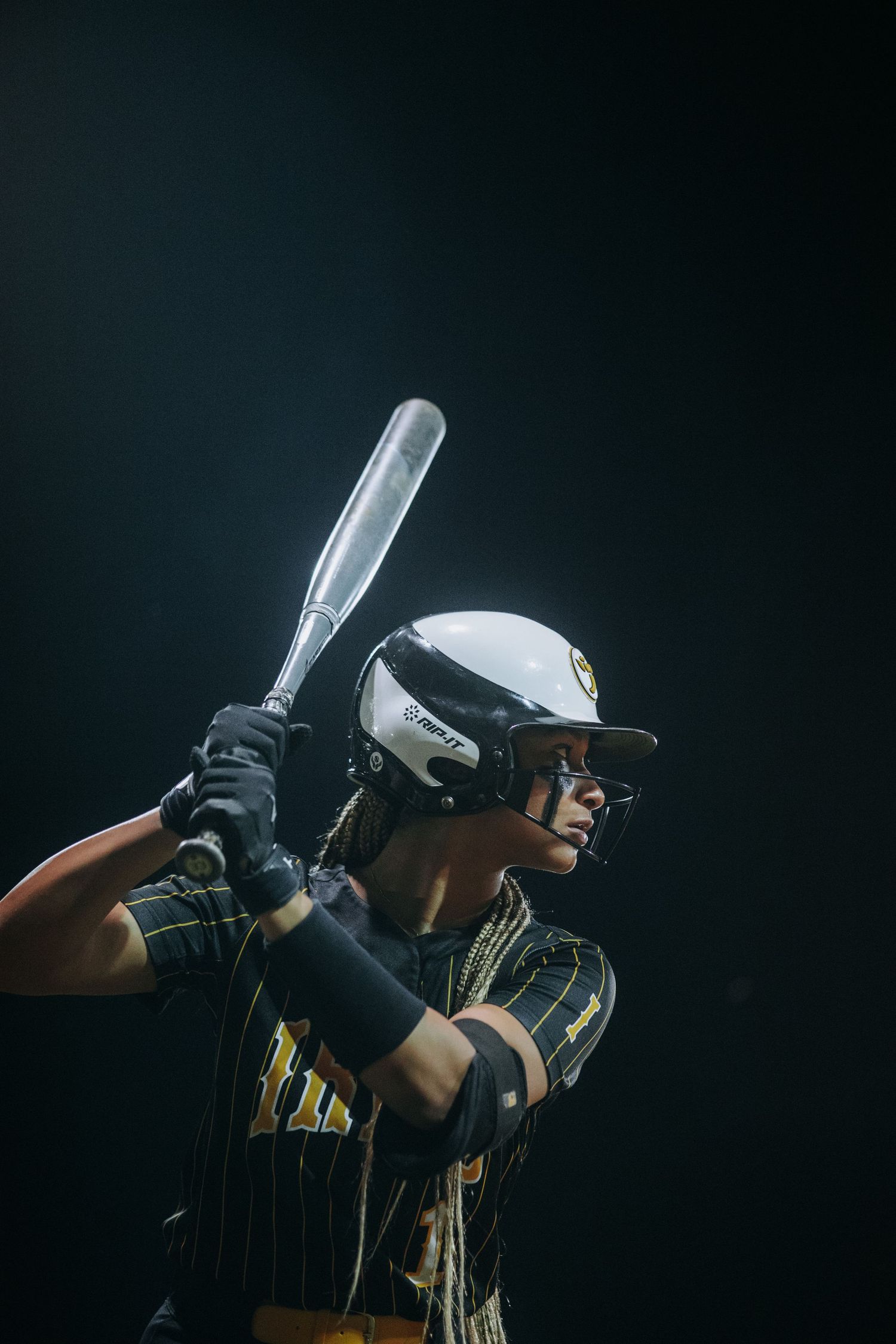 Baseball player in pinstripe uniform takes batting stance against dark background.