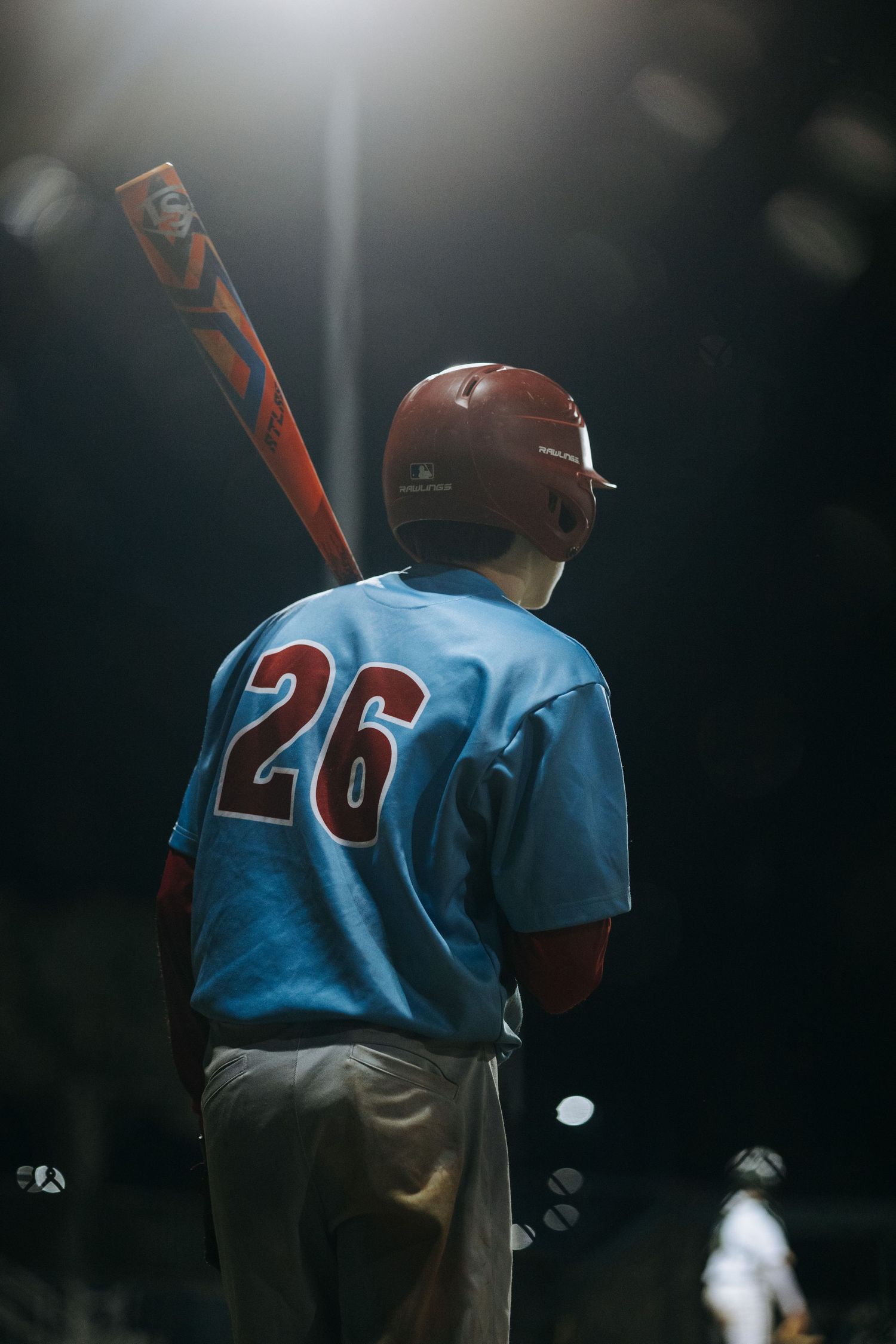 Baseball player wearing number 26 light blue jersey stands at bat under stadium lights.