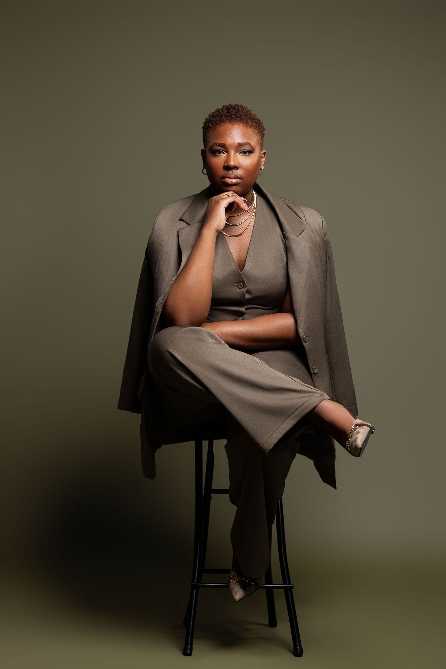 Sophisticated portrait in olive tones featuring model in tailored suit on bar stool.