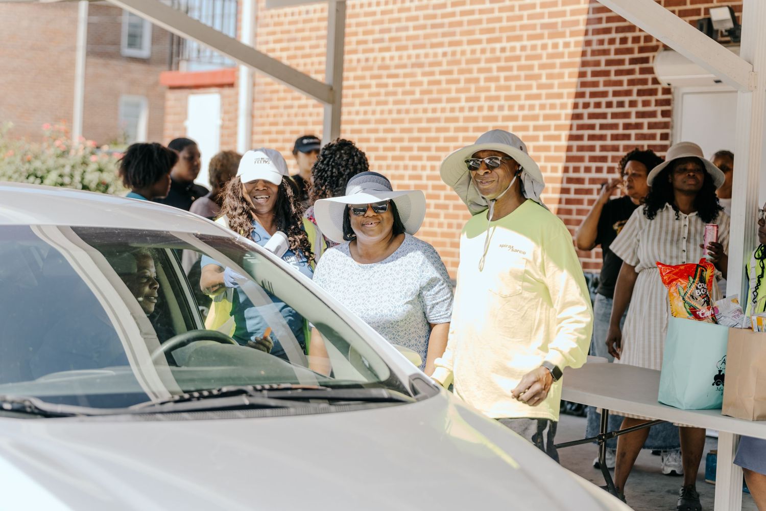 Diverse group of people gathered outdoors near a brick building at a community event on a sunny day.