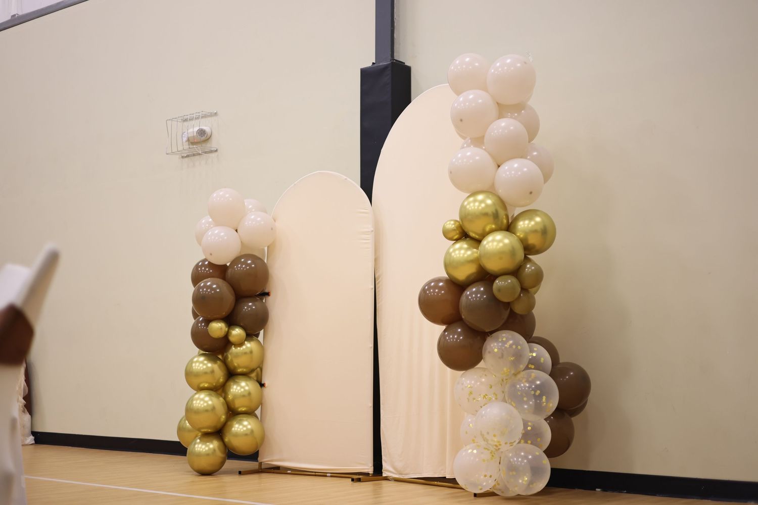 Gold, brown, and white balloon garland decorating two arch panels at an event venue.