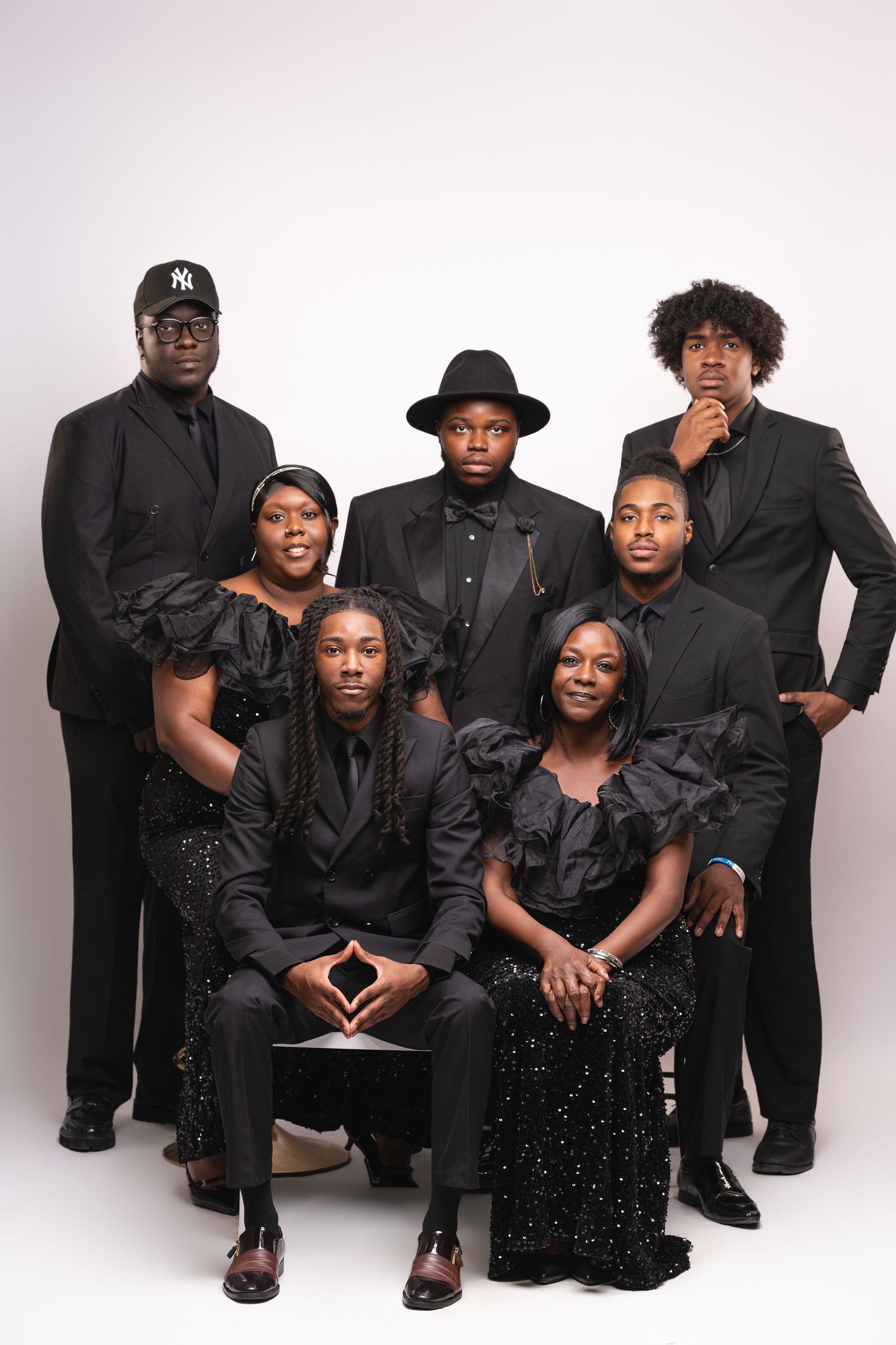 A group of six people pose together in formal black attire against a light background for a studio portrait.