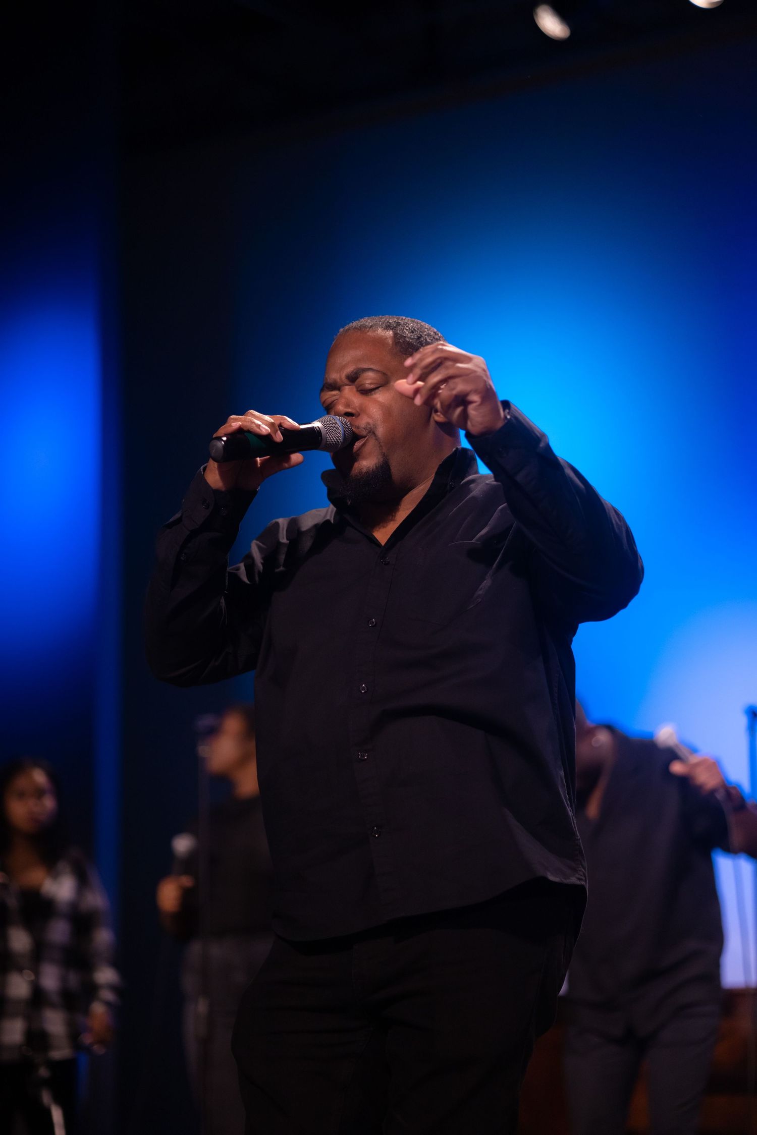 A performer sings passionately against a blue-lit backdrop during a worship service.