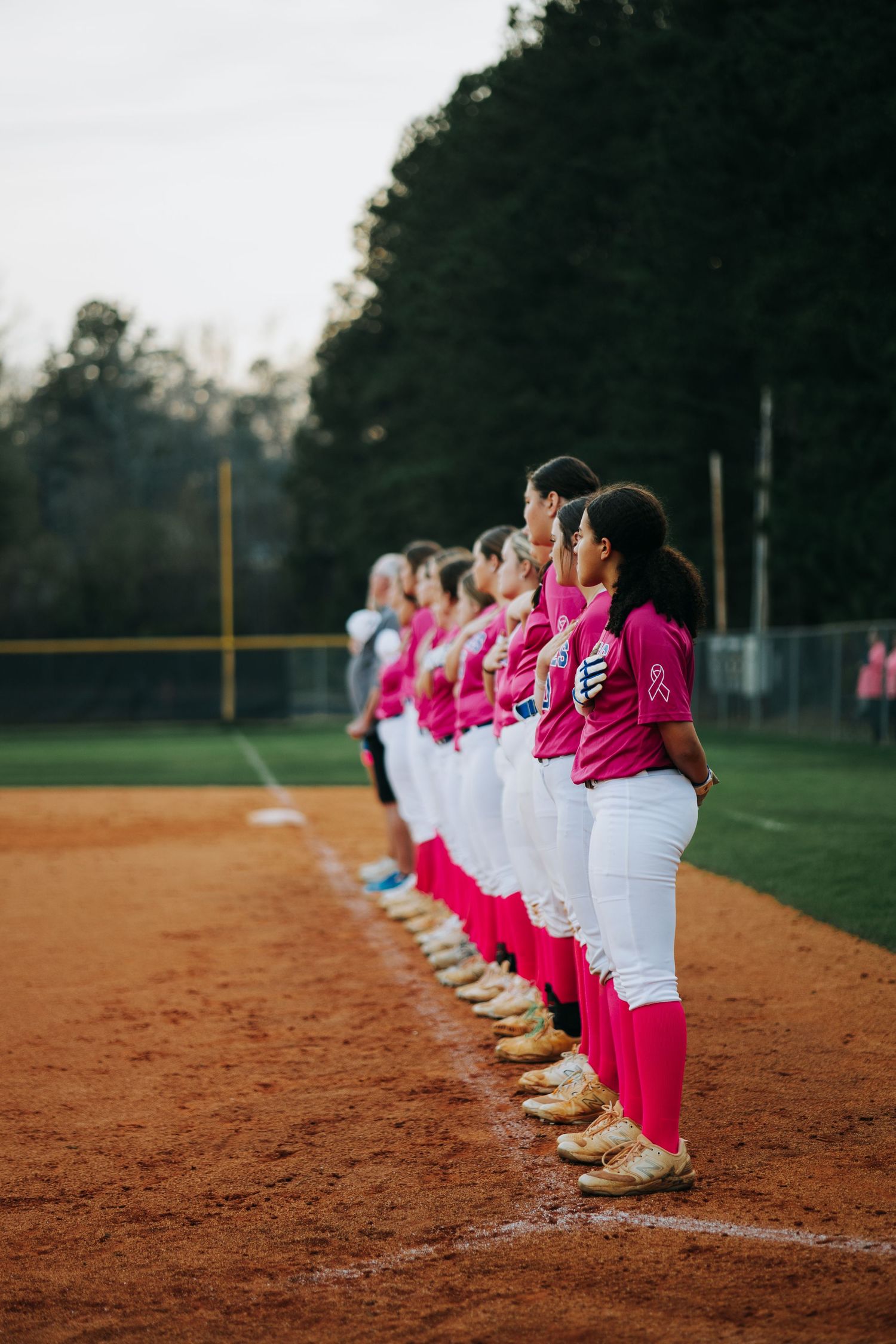 Softball team performing synchronized stretching routine on dirt infield.
