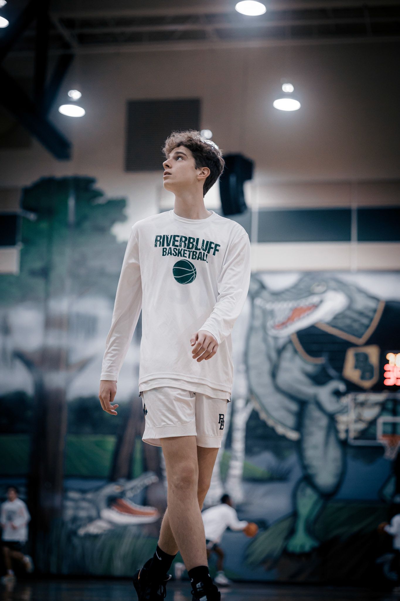 Basketball player wearing white Powerhouse shirt stands in indoor gym.
