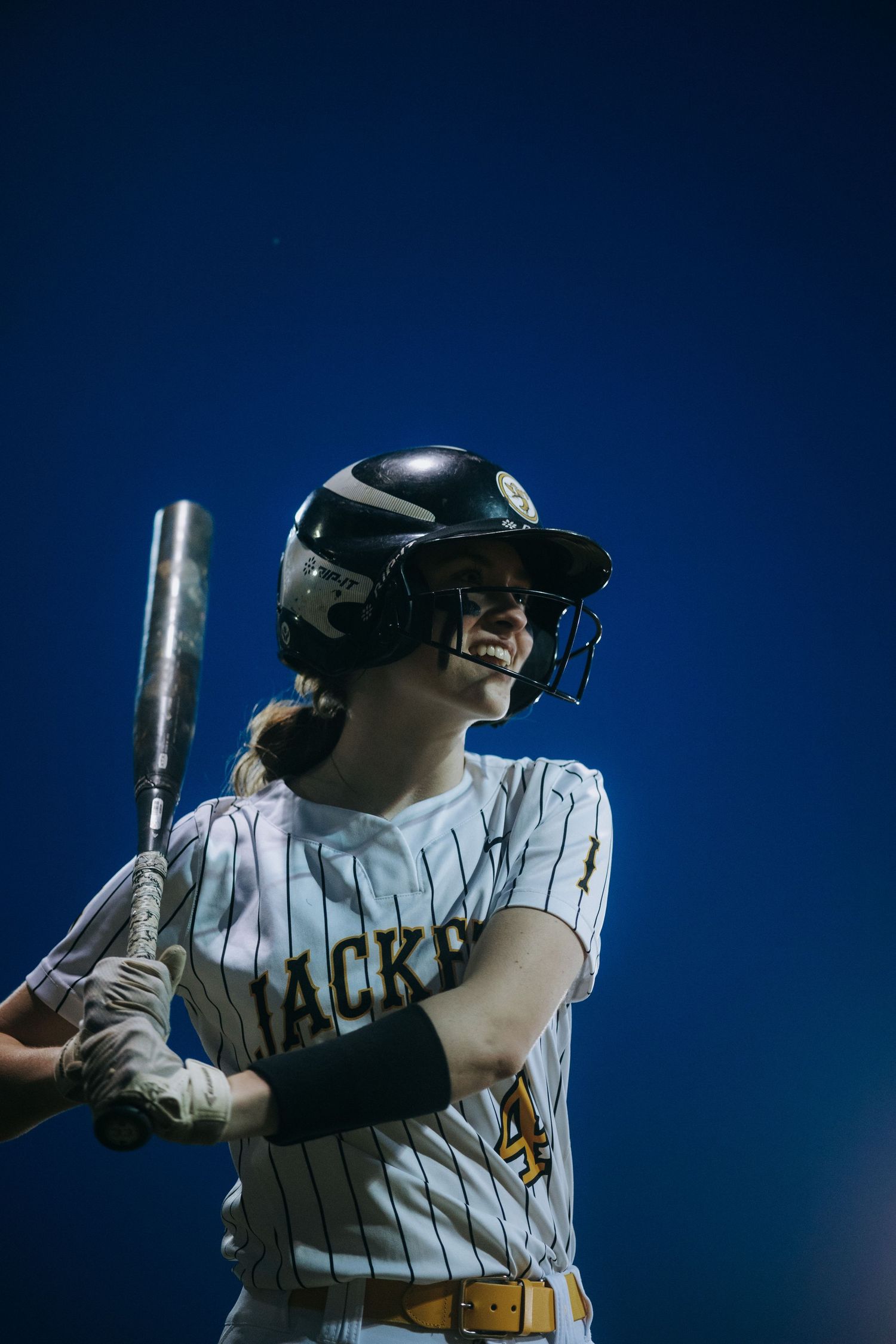 Baseball player in pinstriped jersey takes batting stance against deep blue sky.