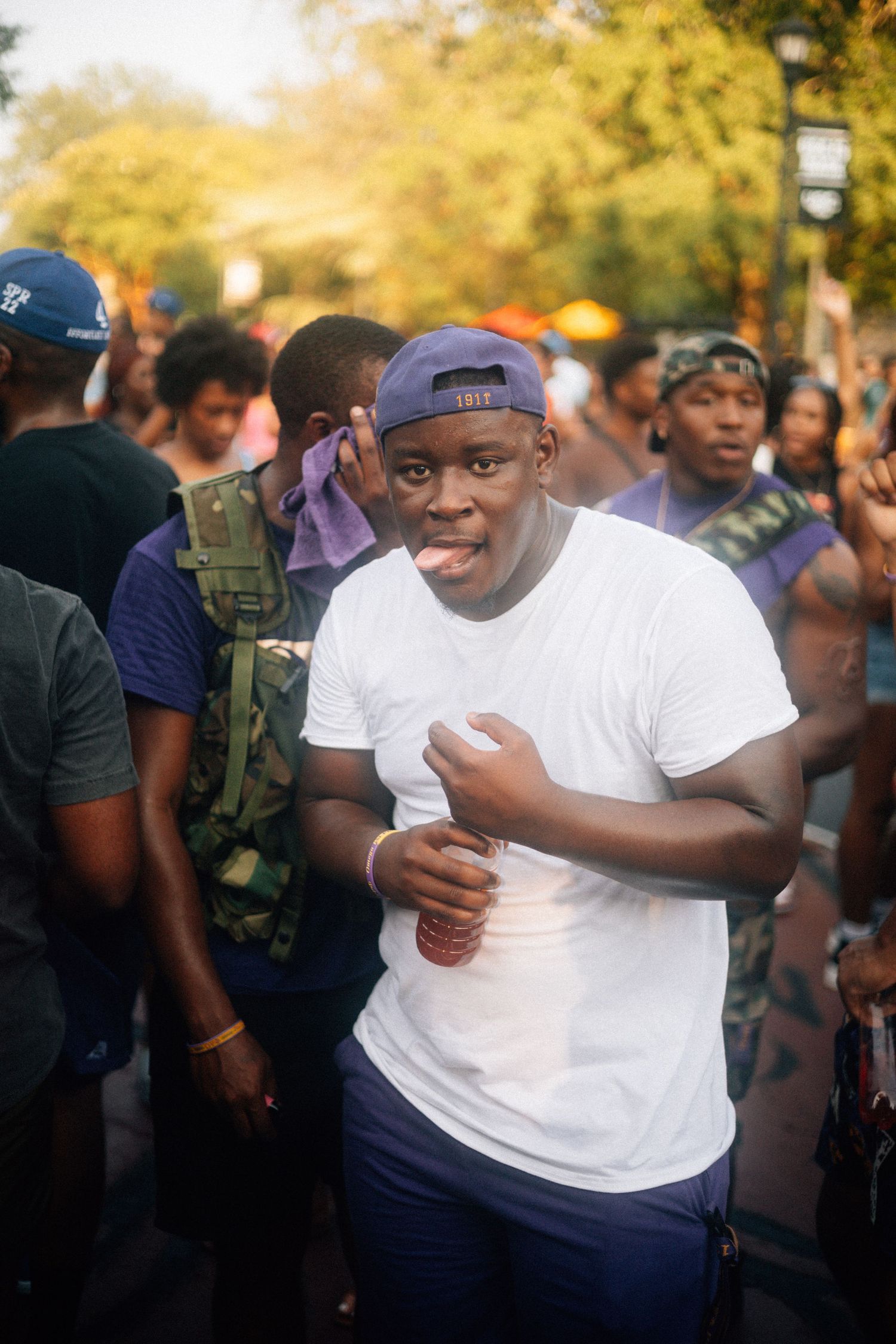 A QUE DAWG in a white t-shirt is seen making facial expressions in a series of candid photos at an outdoor gathering.  USC Hip Hop Wednesday