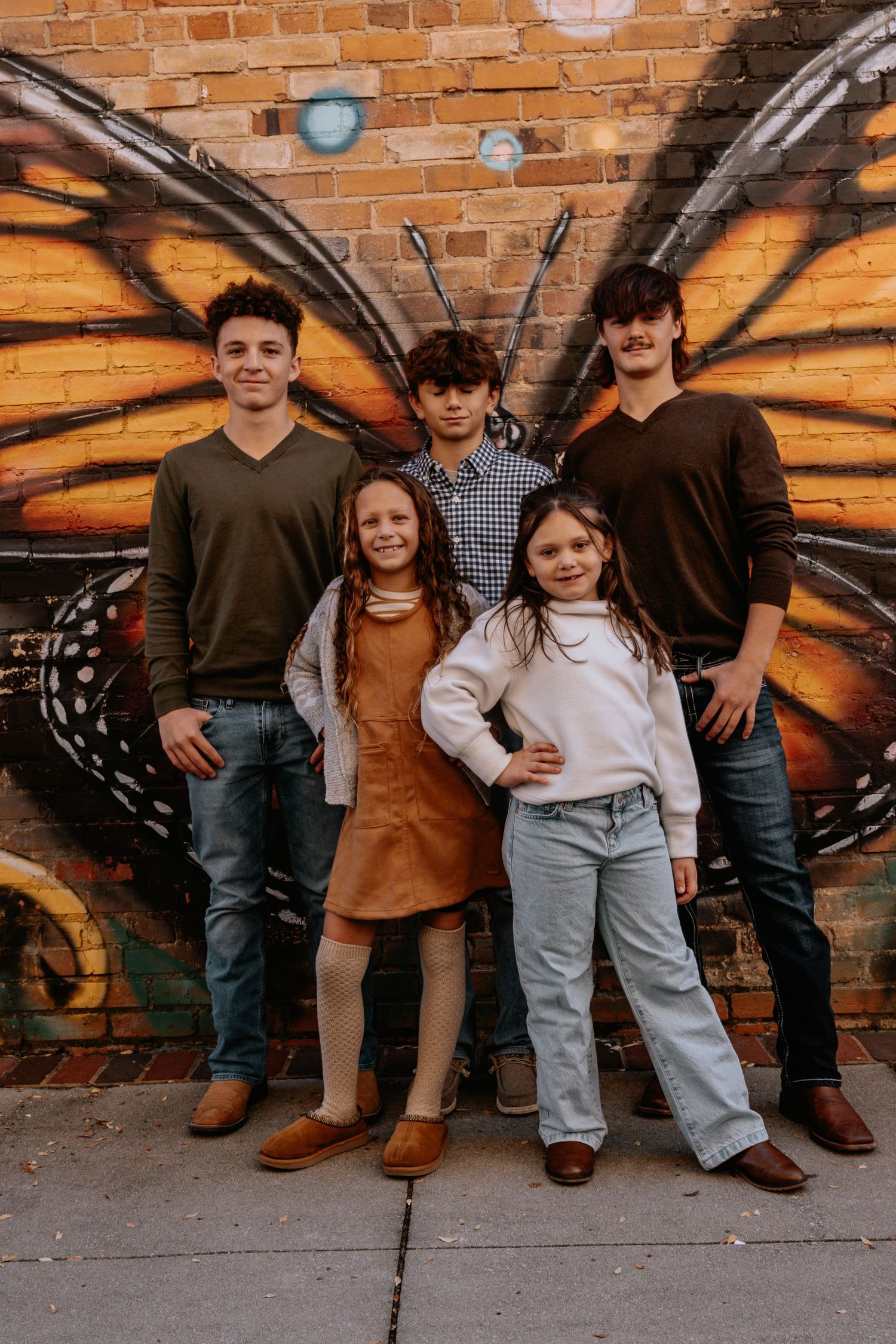Group photo of young people posed in front of a vibrant butterfly mural on brick wall.