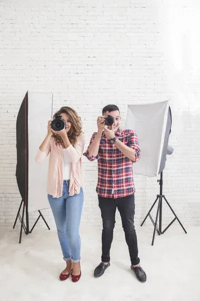 Two photographers in studio setting taking pictures with professional cameras and lighting equipment.