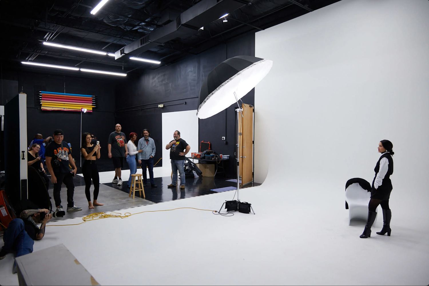 Behind-the-scenes view of a professional photo studio with white walls, lighting equipment and crew members working.
