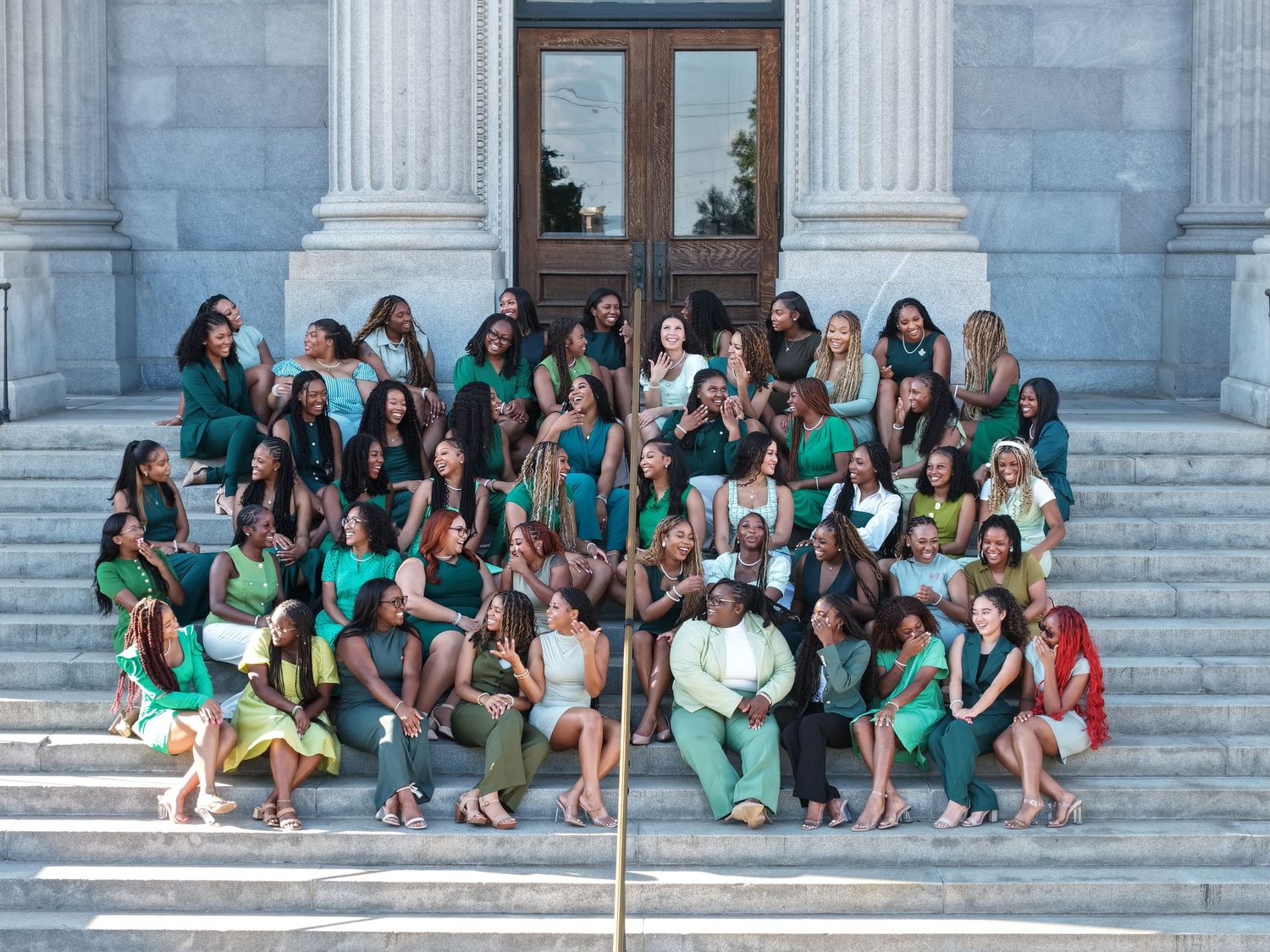 A large group in matching outfits sits for photos on white stone steps of a building entrance.