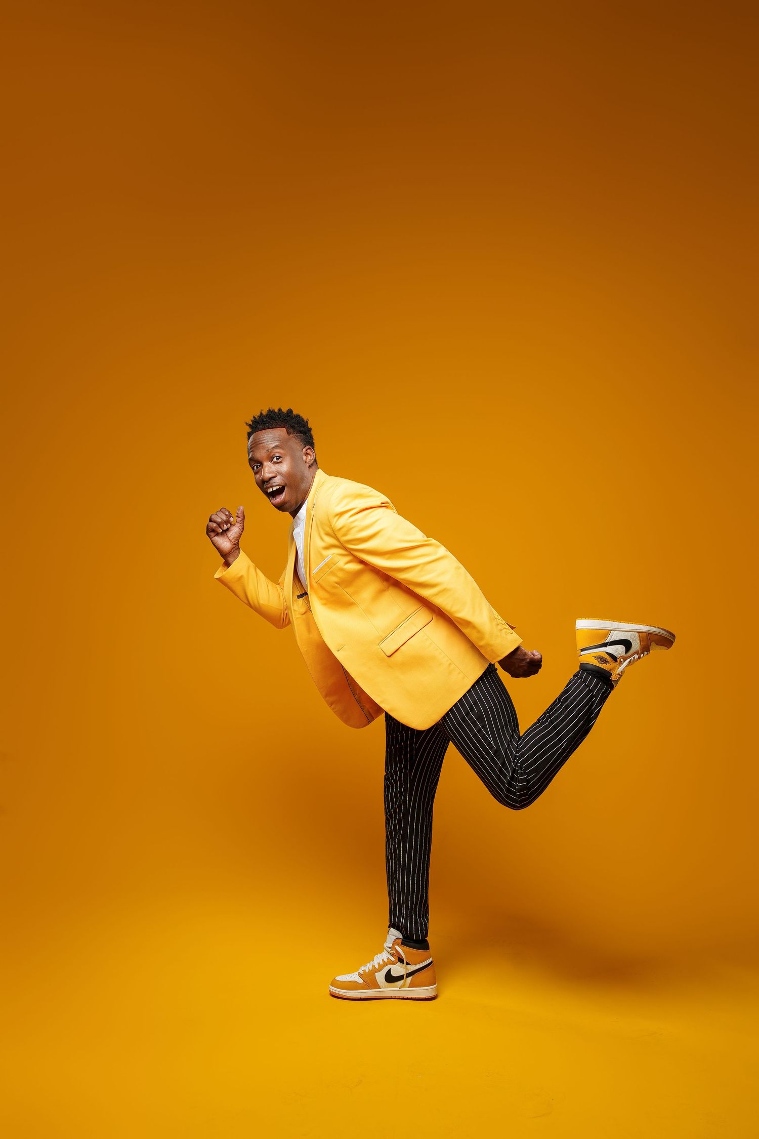 Person in yellow blazer and striped pants performs dynamic dance poses against vibrant orange backdrop.
