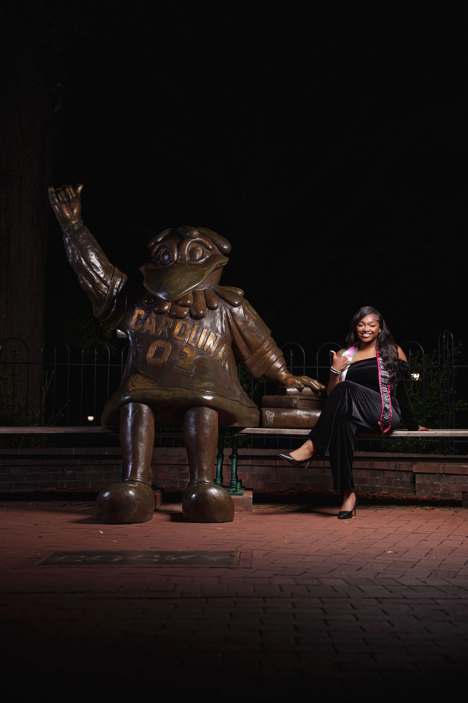A series of nighttime photos showing someone posing playfully with a large bronze sculpture on a brick walkway.