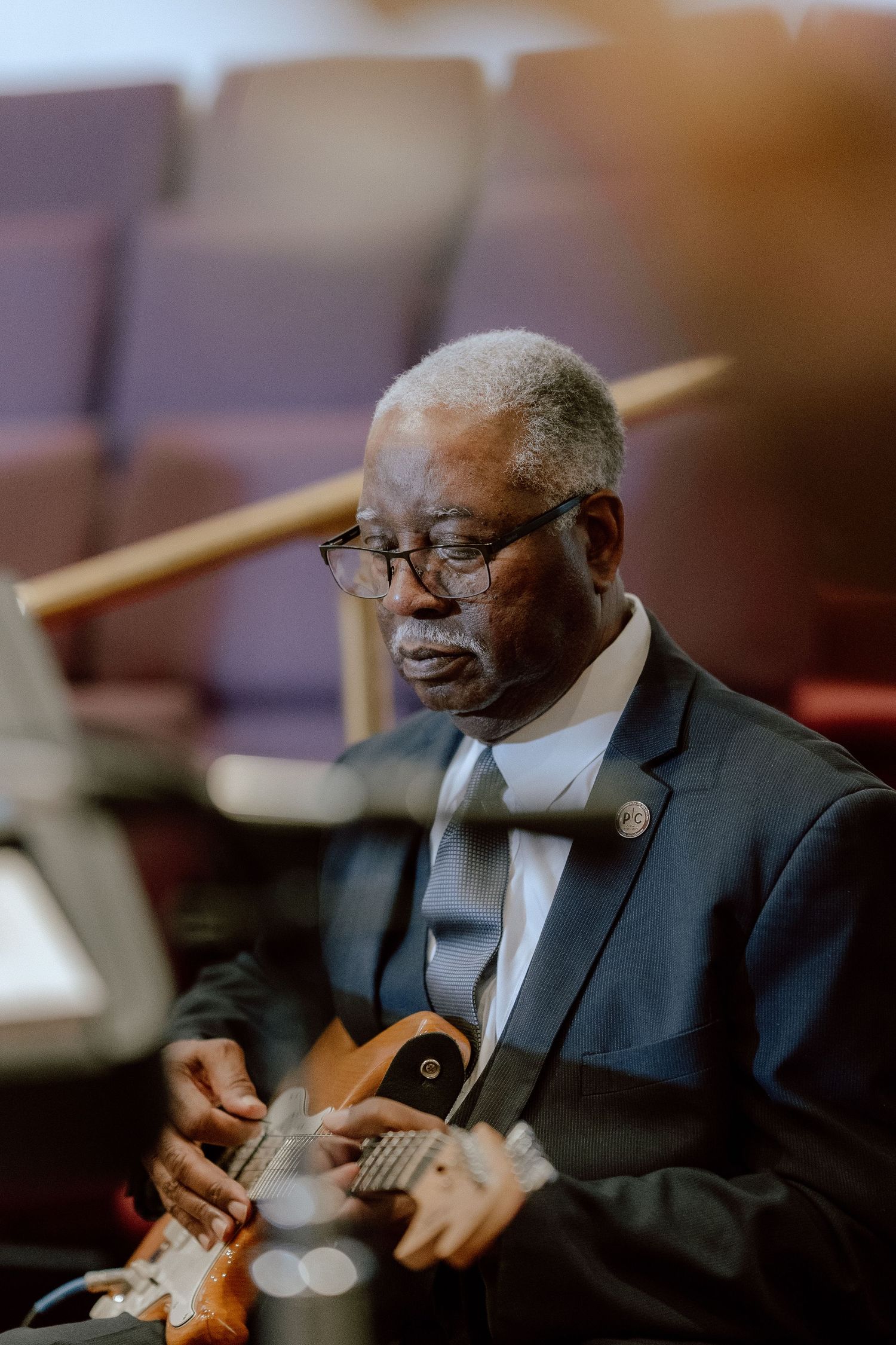 A person in a dark suit plays a guitar in a warm-lit room, shown in a series of sequential shots.