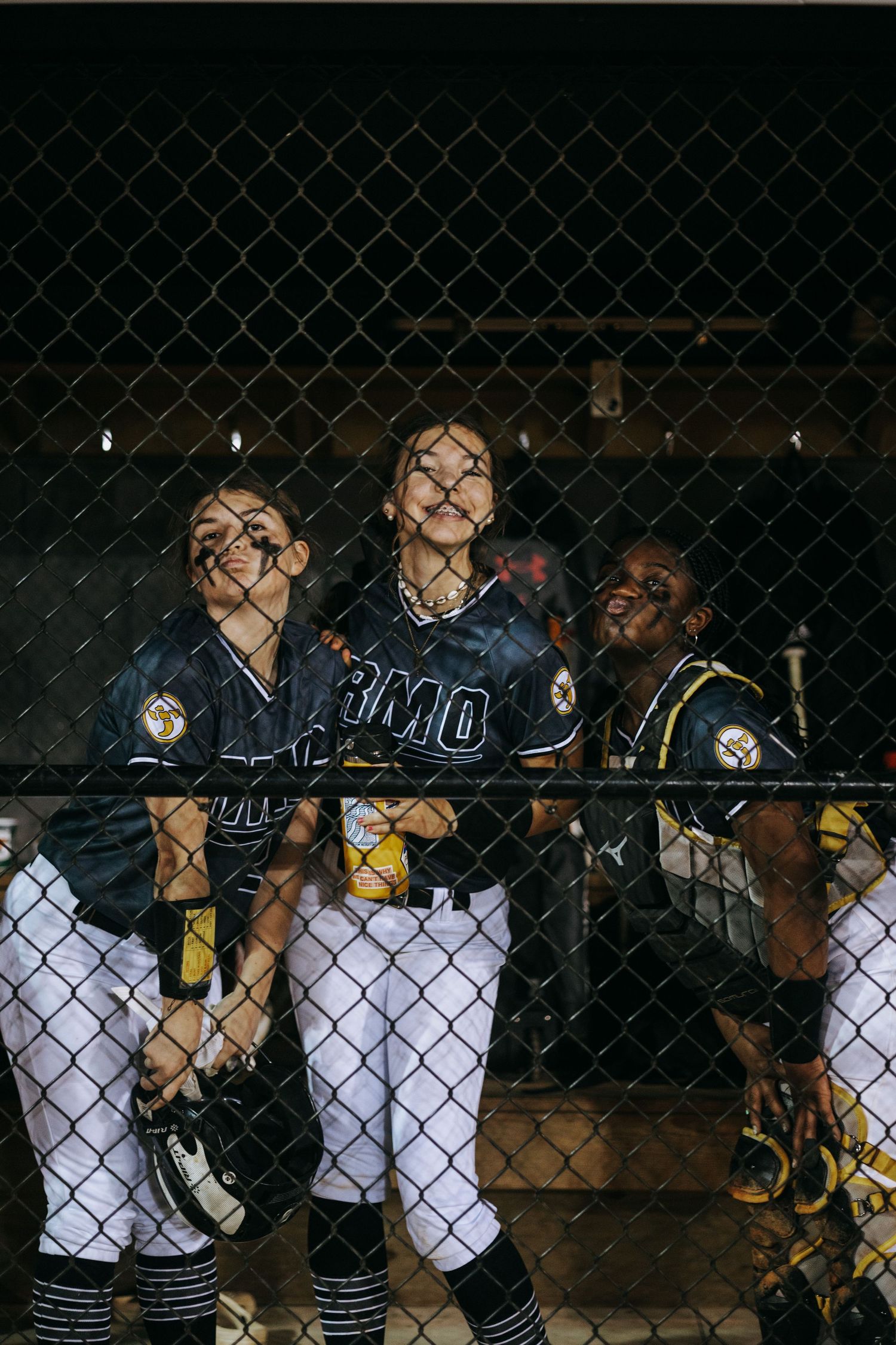 Softball players in navy uniforms look through chain link fence during night game.