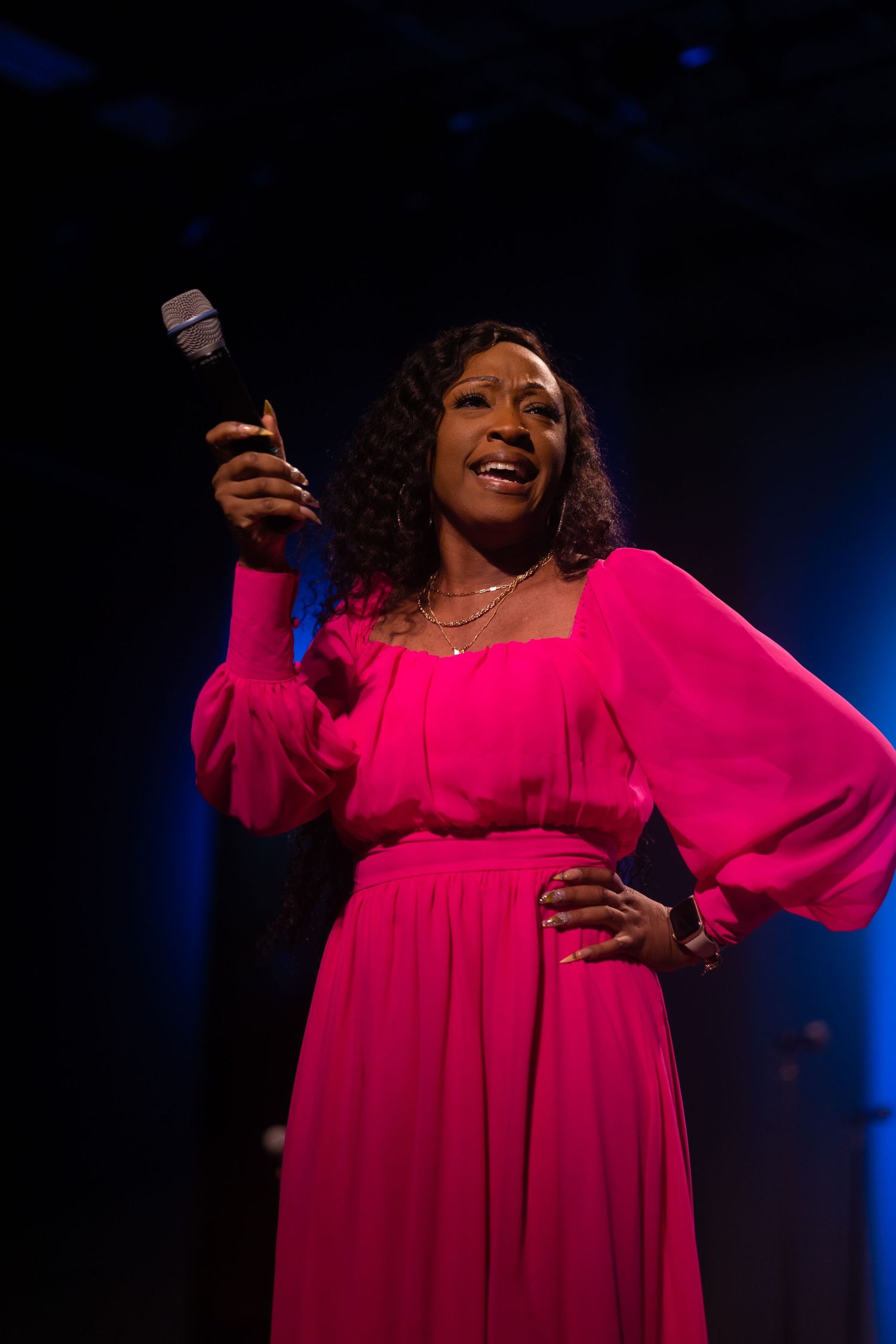 A singer in a vibrant pink dress performs on stage with dramatic lighting.