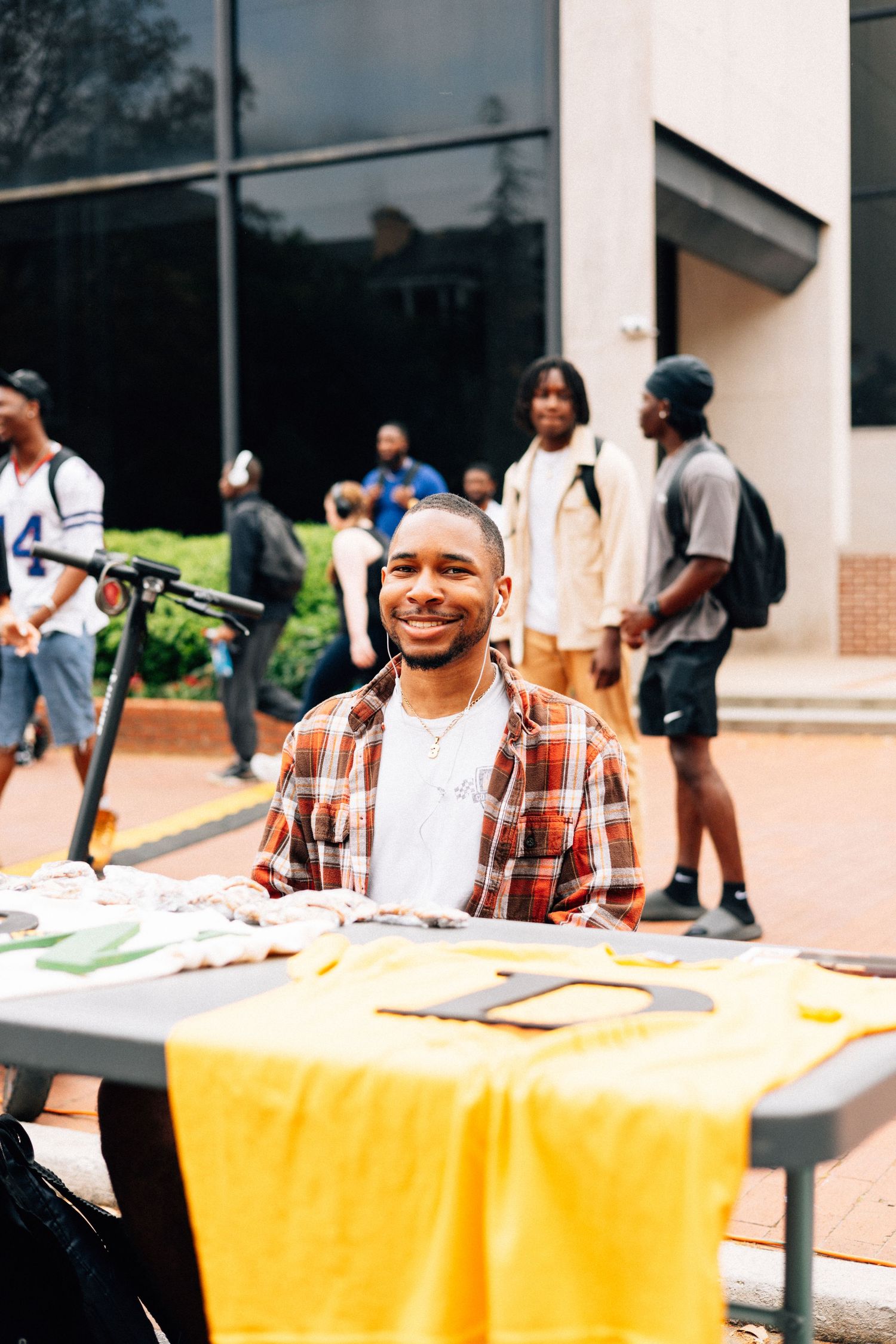 College students visit tables at a campus club fair and activity expo with yellow tablecloths outdoors.