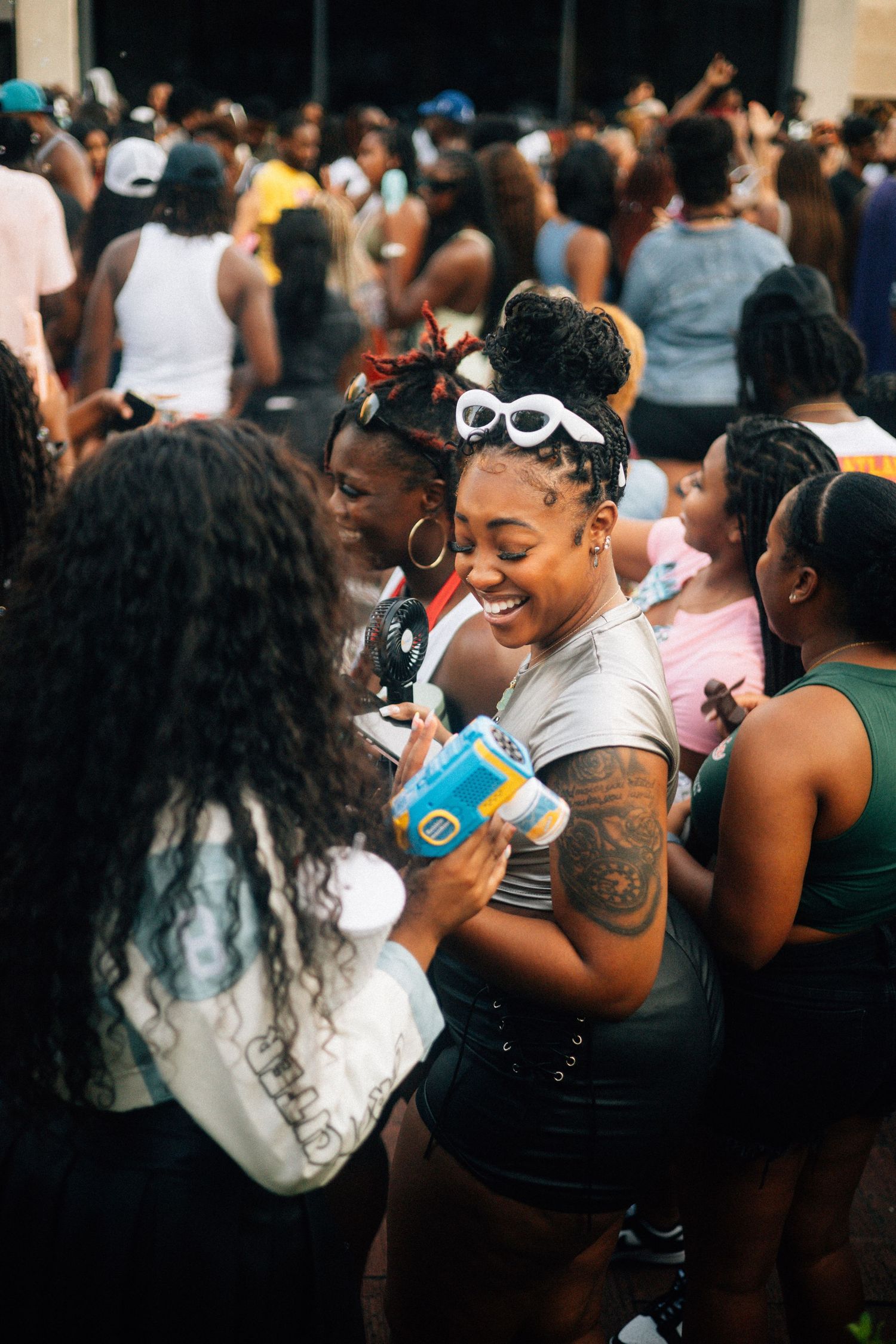 A crowd of people enjoy a lively outdoor gathering with drinks and festive white goggles on a sunny day. USC Hip Hop Wednesday