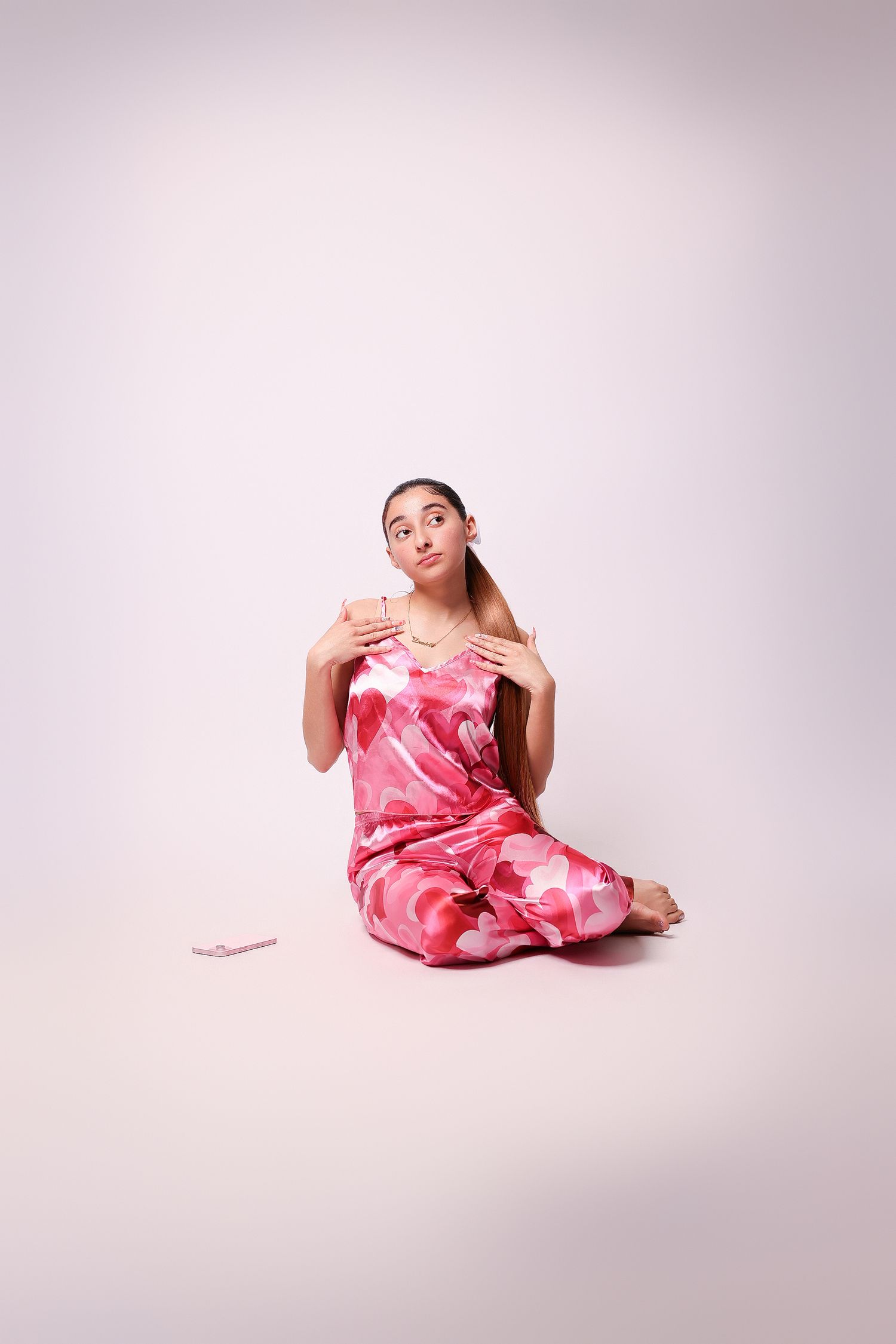 Figure in pink patterned dress sits gracefully on floor against light background in artistic pose.