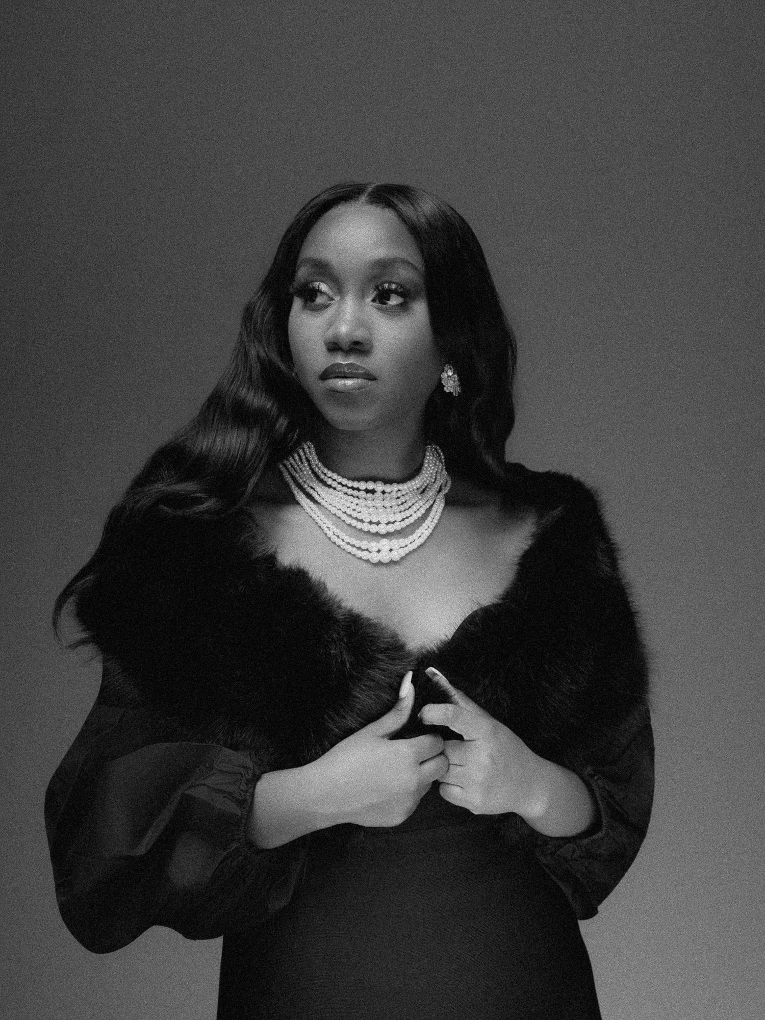Black and white portrait of a woman in fur wrap and layered pearl necklace, elegant fashion photography.
