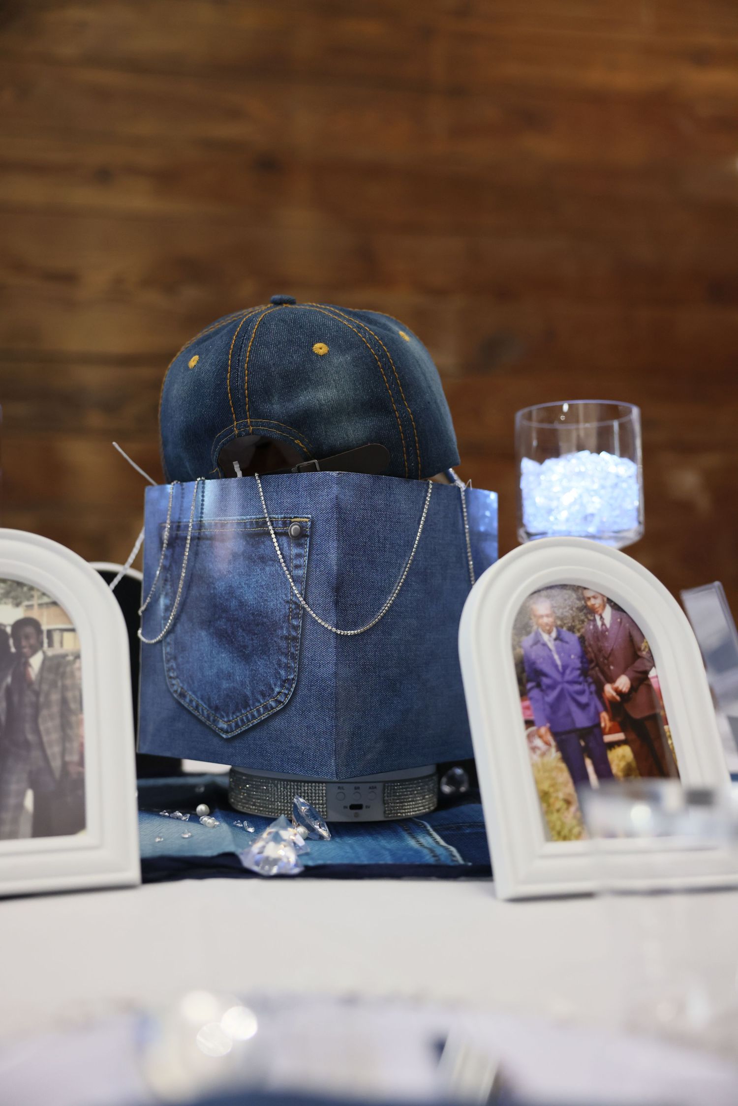 Denim centerpiece with blue cap, framed vintage photos, and glass vase on decorated table at memorial event.