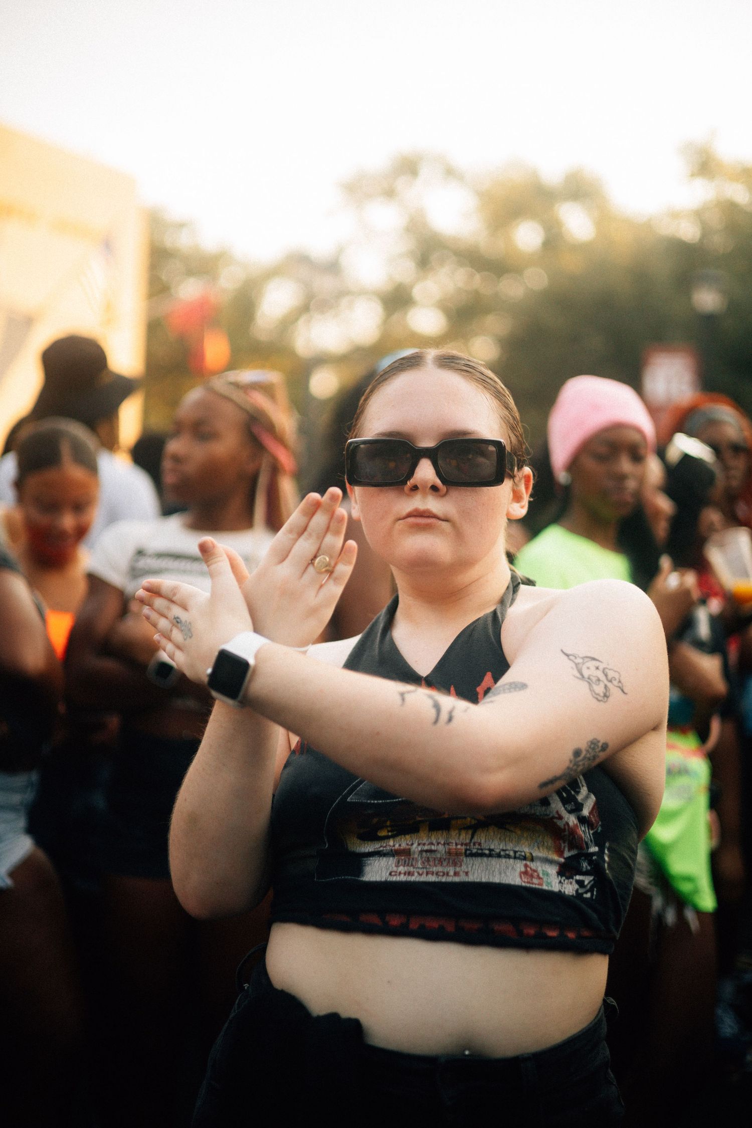 Person in black shirt and sunglasses raises arms outdoors at sunset during a crowded event.USC Hip Hop Wednesday