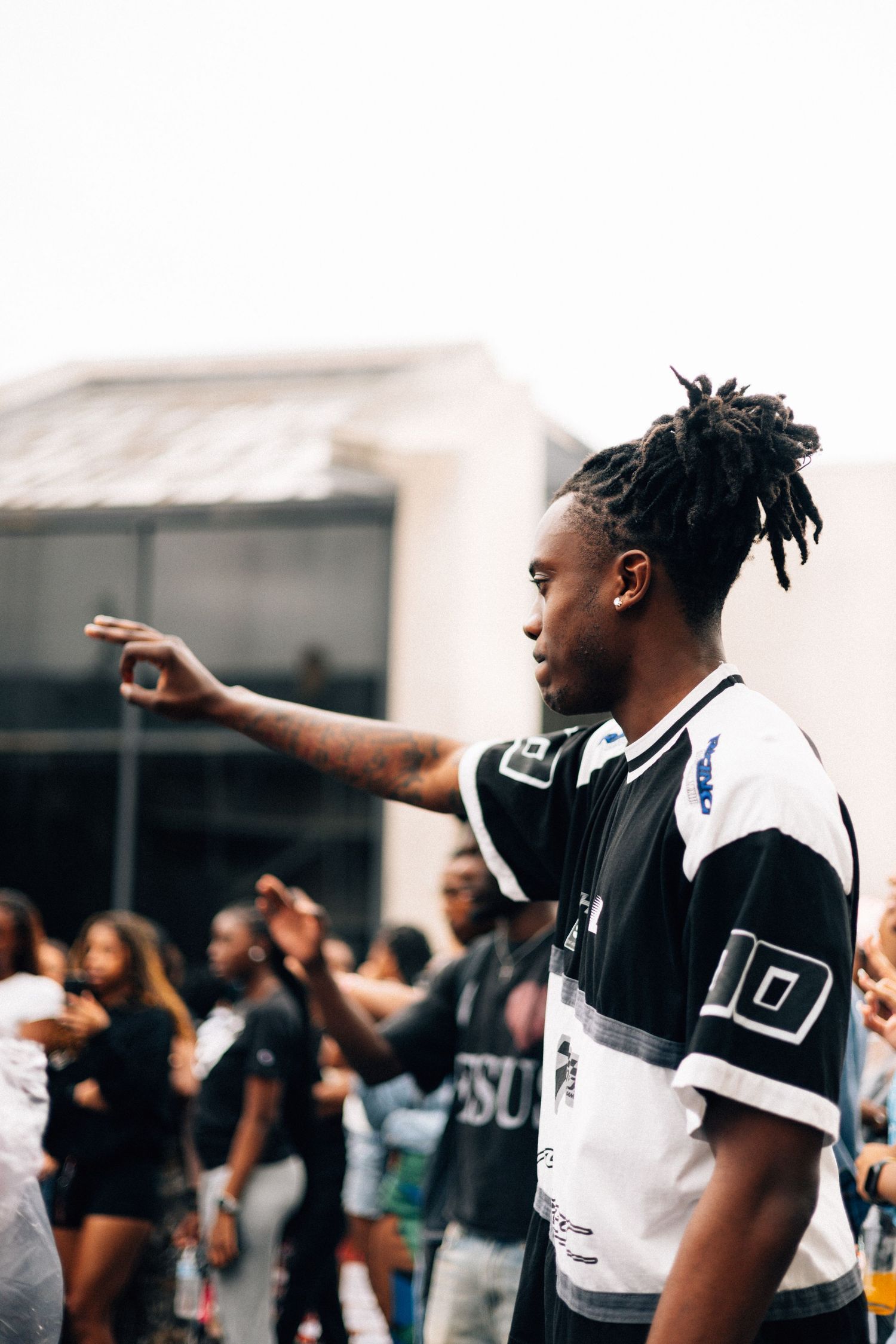 A person in a black and white jersey gestures while standing among a crowd at an outdoor event.