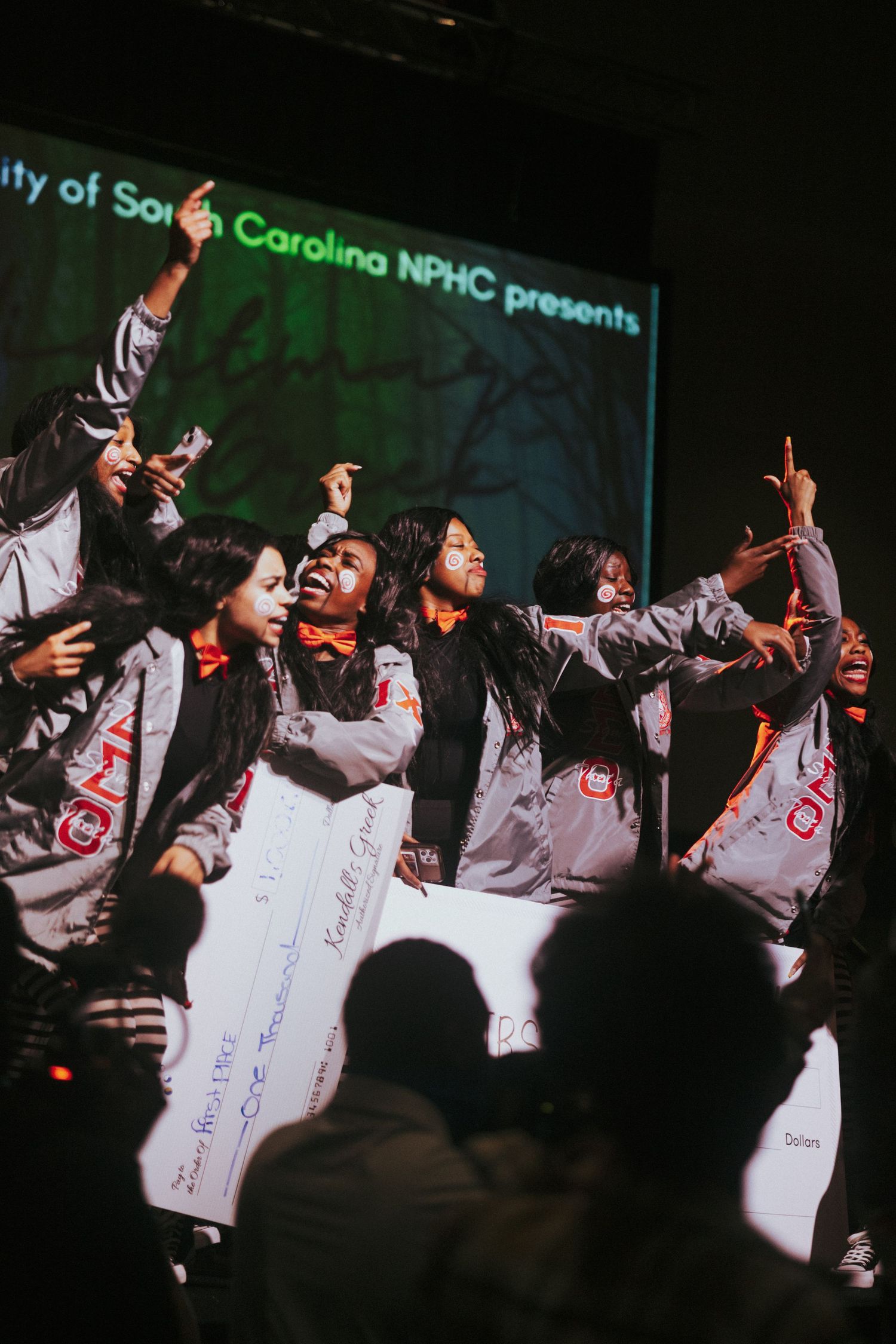 Deltas dancing energetically on stage wearing matching white outfits during a South Carolina NPHC presentation.