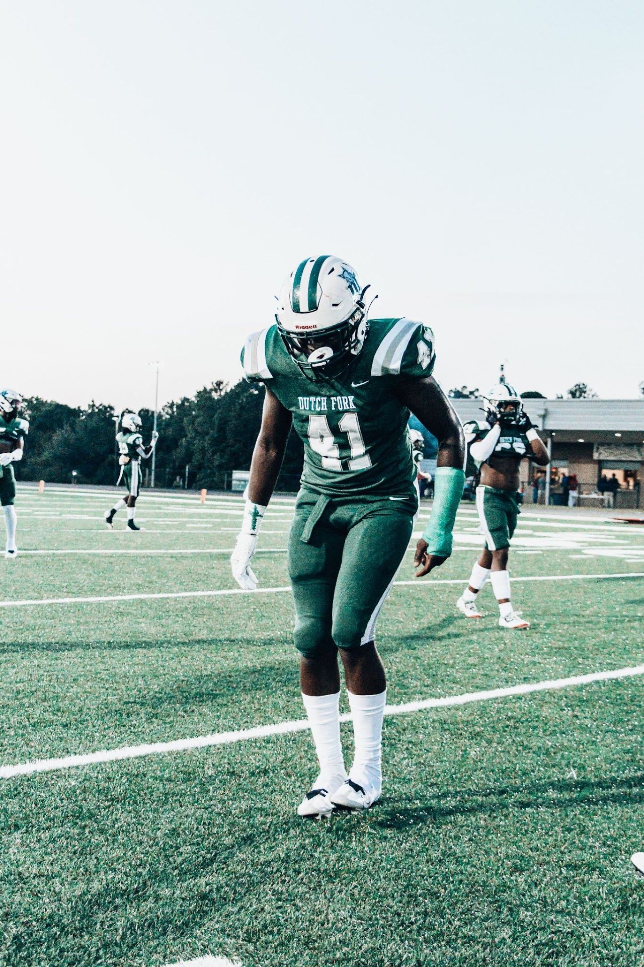 Football player in green and white uniform stands on field during practice or game.  DFHS