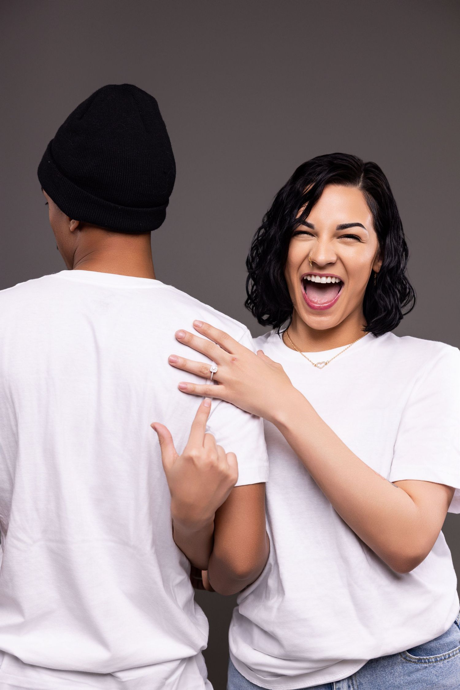 A joyful interaction between two people wearing white t-shirts against a gray background.