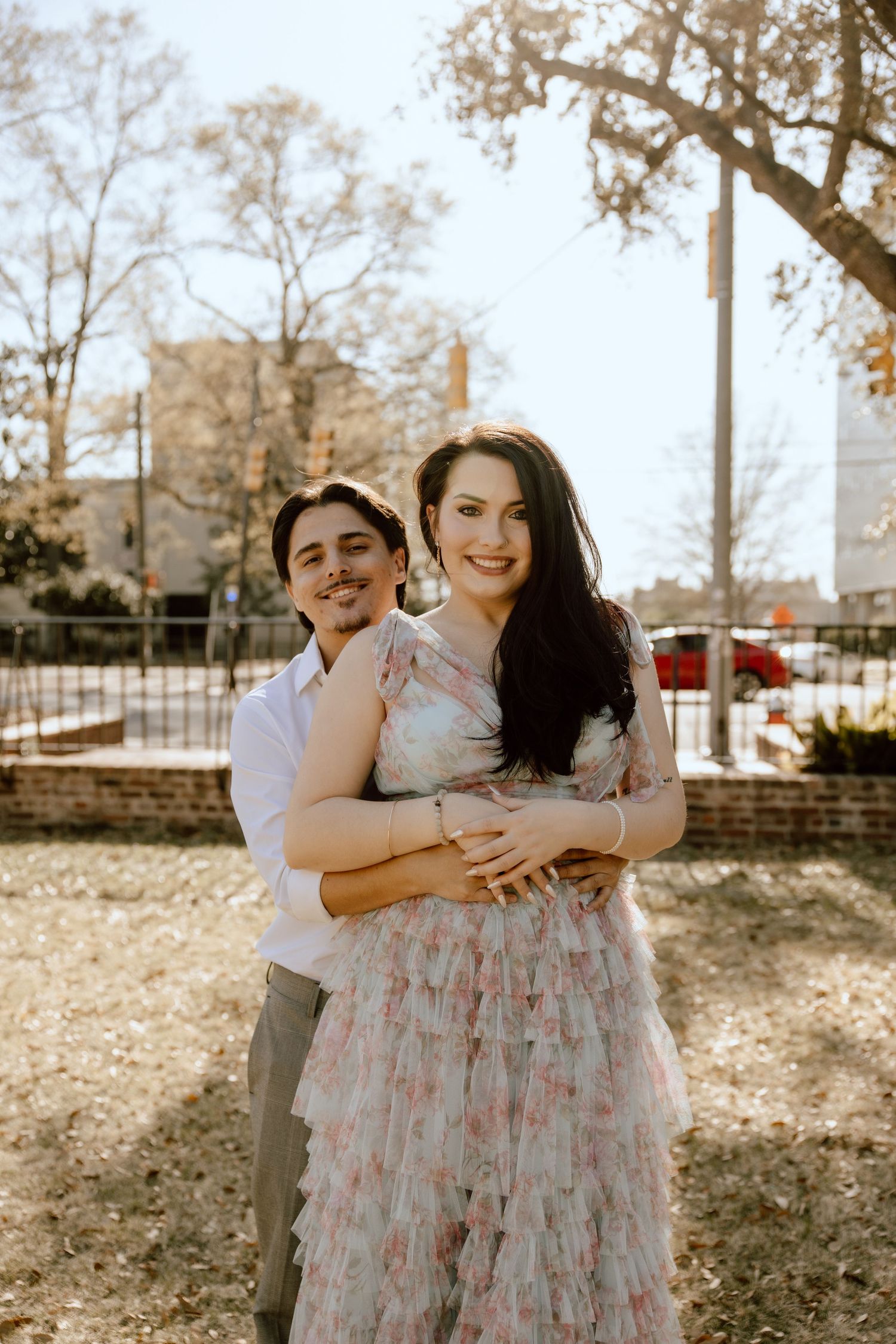 Couple shares intimate embrace in floral dress and white shirt outdoors.