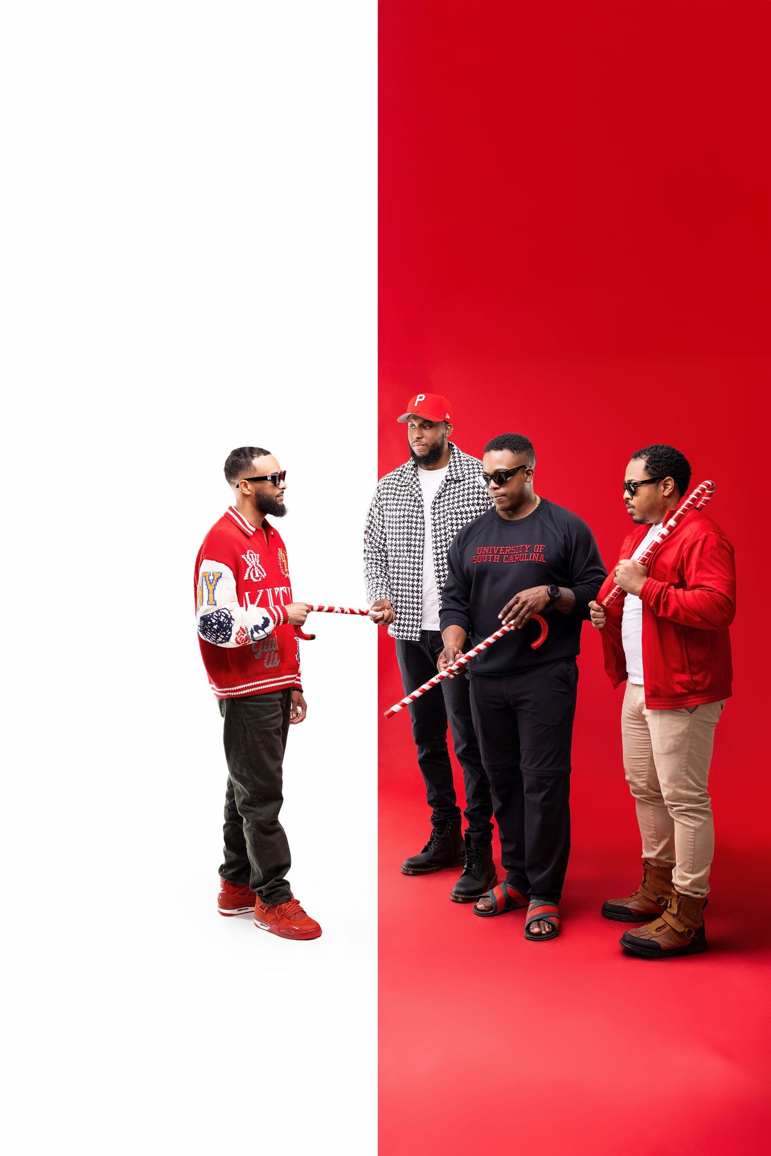 Four people in casual wear pose with hockey sticks against a split red and white background.