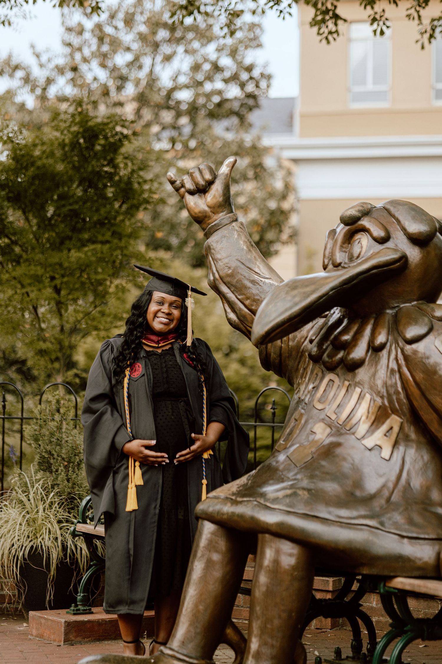 Graduate posing with campus bronze mascot statue outdoors.