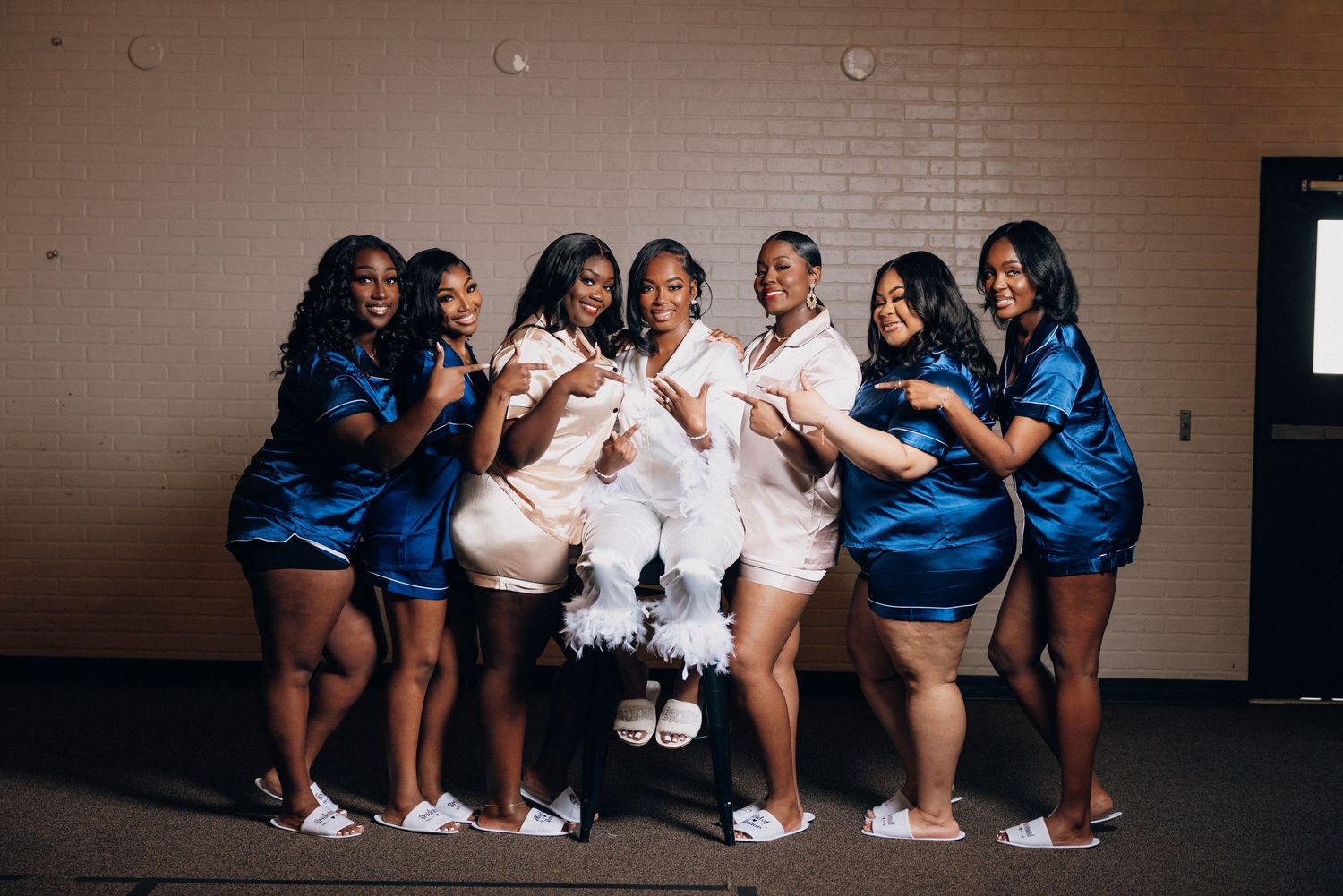 A group of cheerleaders in blue and white uniforms perform synchronized poses in a hallway.
