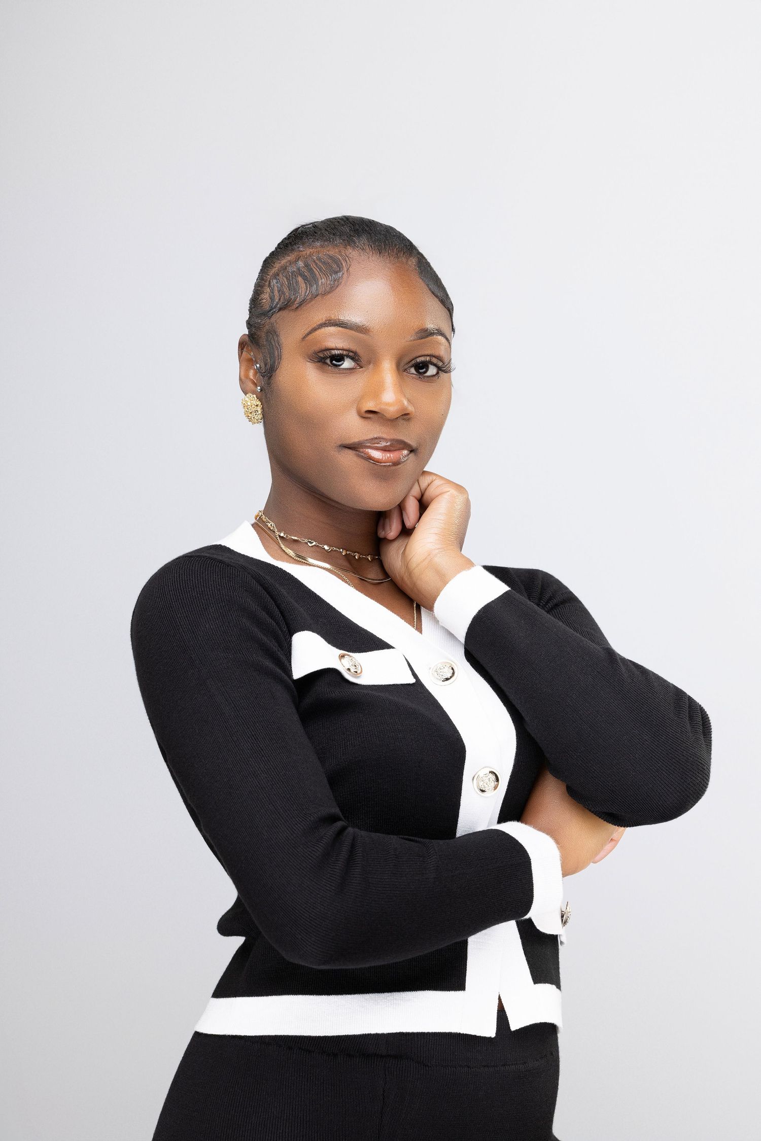 A person in a black and white business outfit poses confidently against a light gray background.
