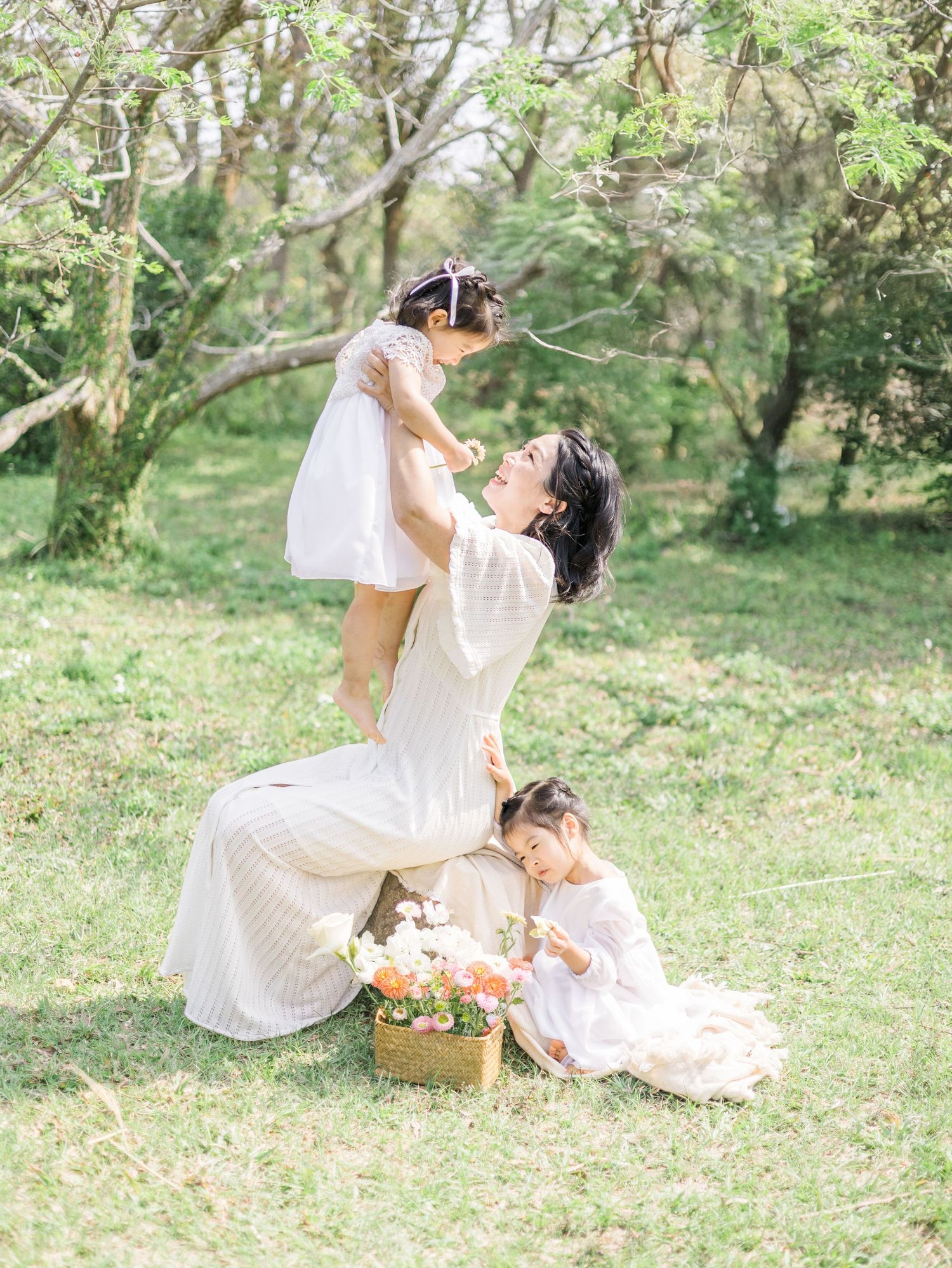 A playful outdoor family scene in white dresses with a picnic basket and flowers in a lush garden setting.