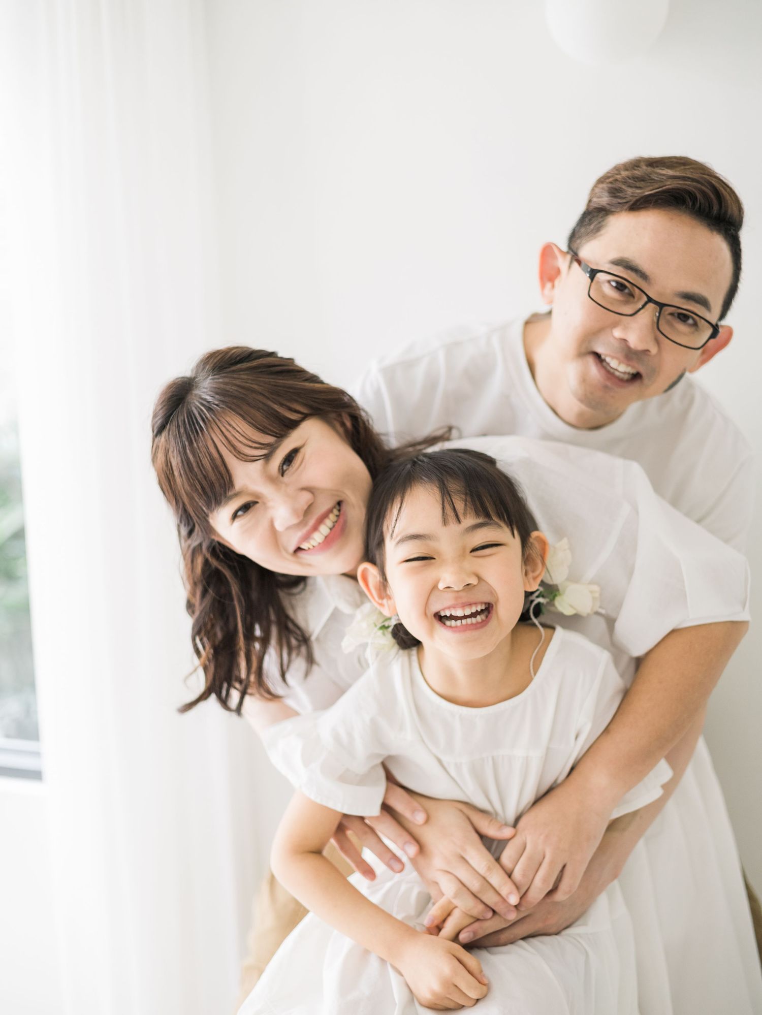 A tender family portrait against a bright white backdrop showing warm embraces and genuine smiles.