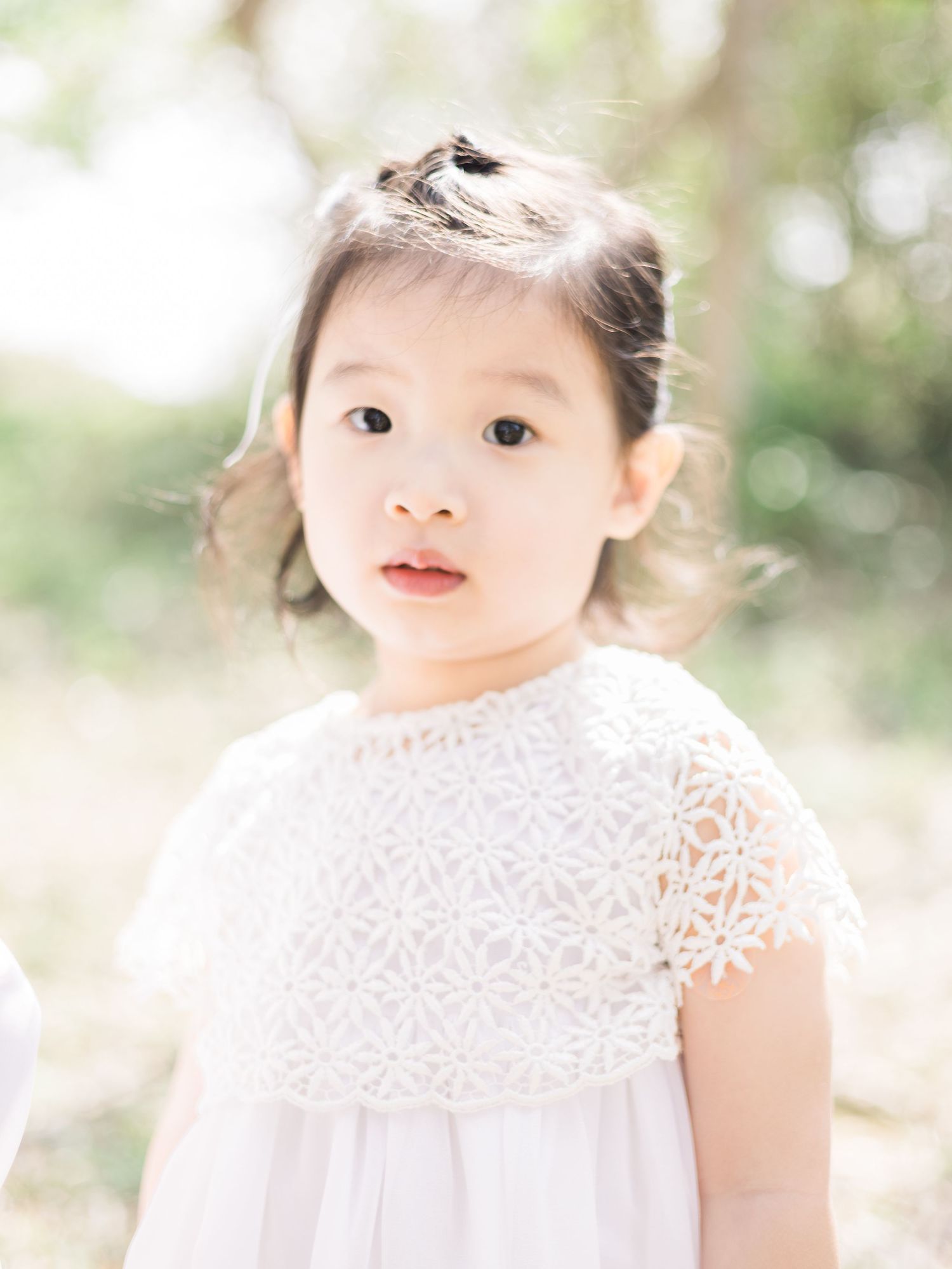 A portrait of a young child in a white lace dress against a soft bokeh background.