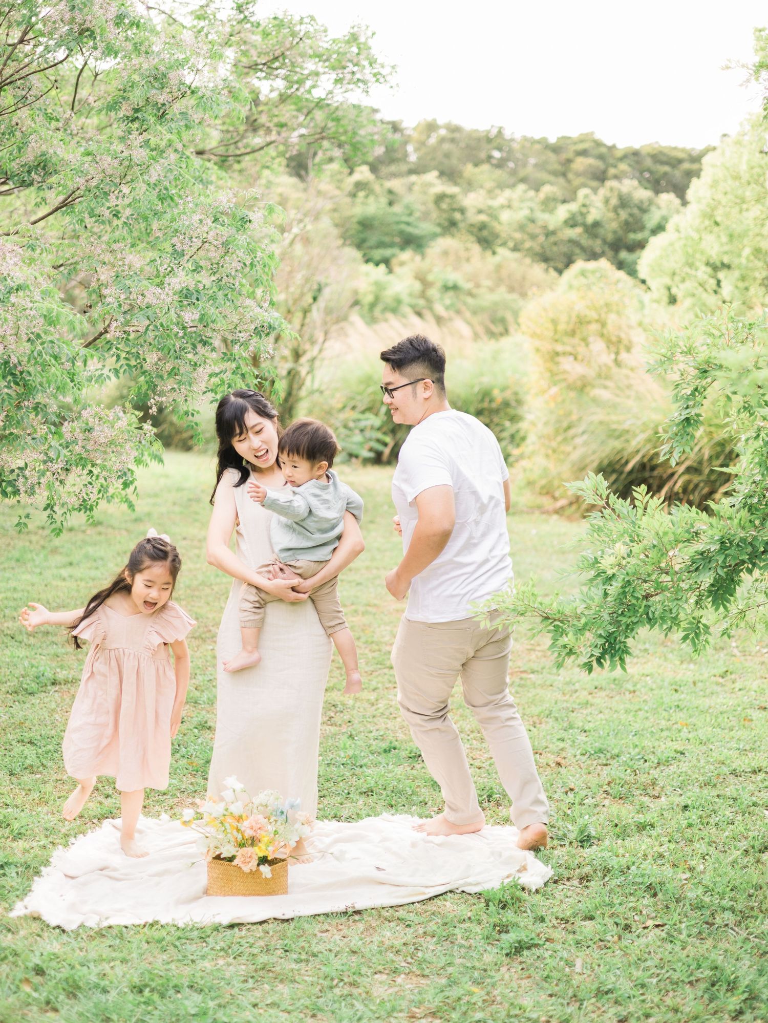 Family standing together on white blanket in a scenic hillside garden setting.