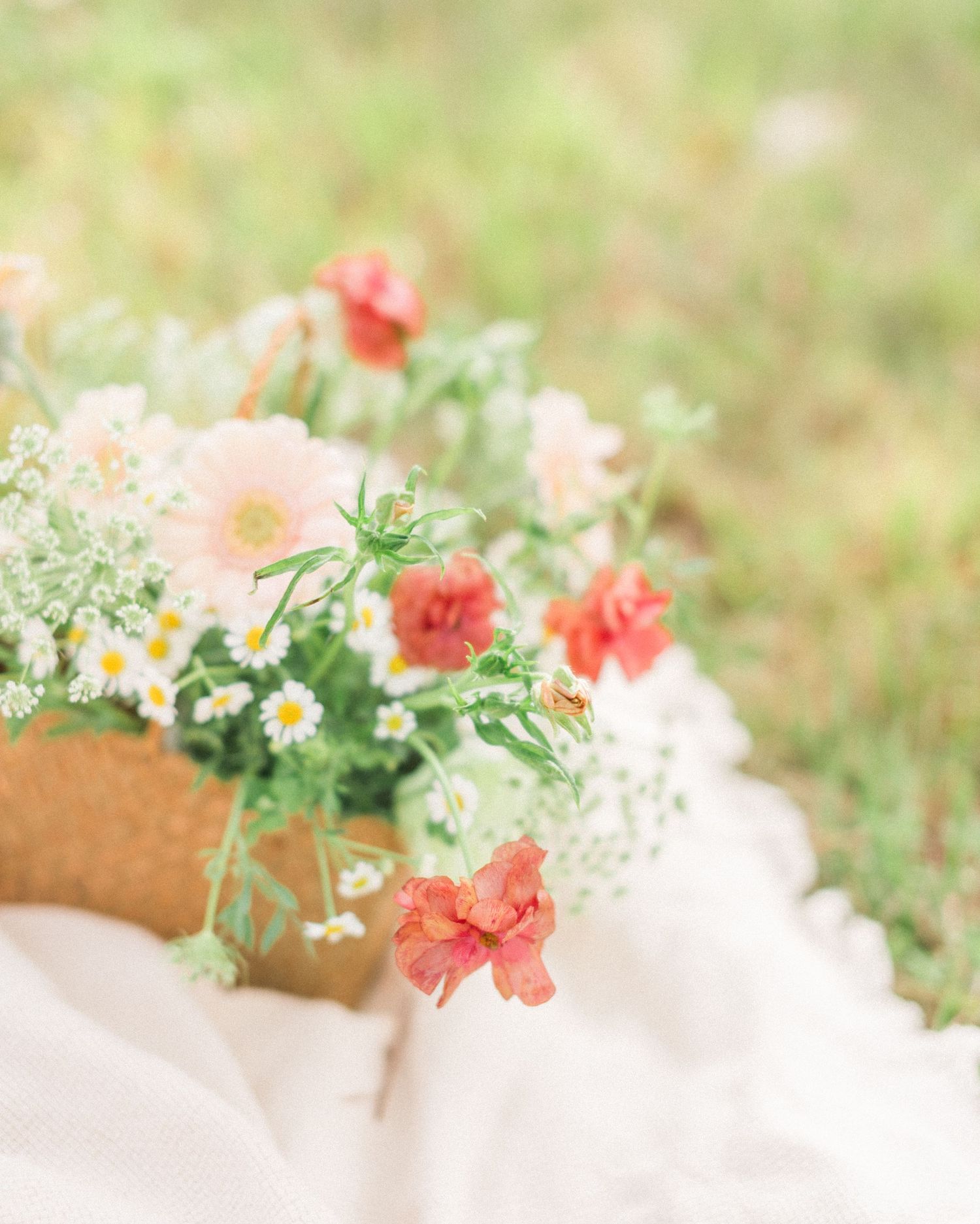 Romantic floral arrangement with coral and pink blooms in a basket against a light fabric.