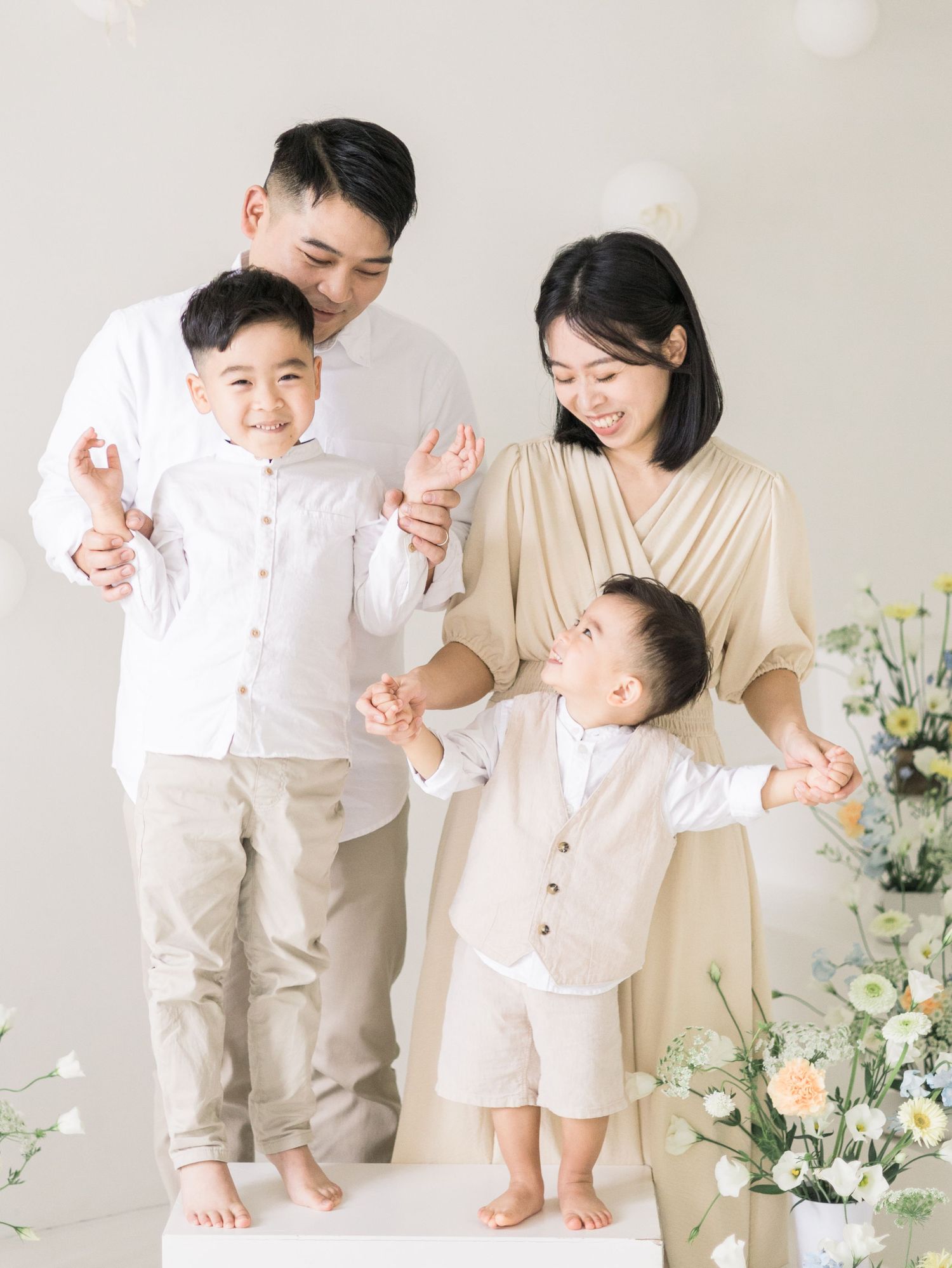 A tender family moment in coordinated white and beige outfits against a light background with floral decor.