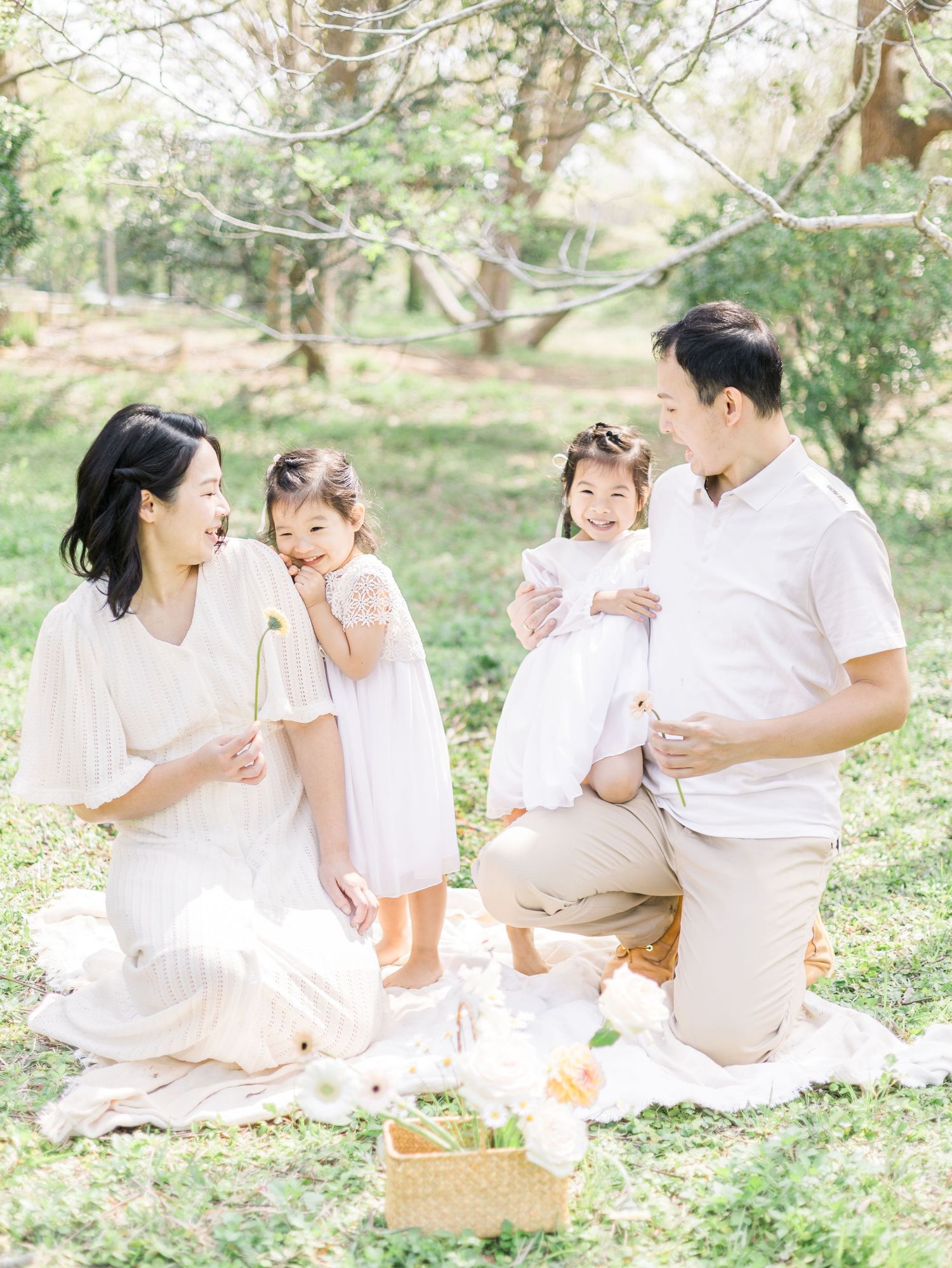 Family having picnic on white blanket in sunny park setting.