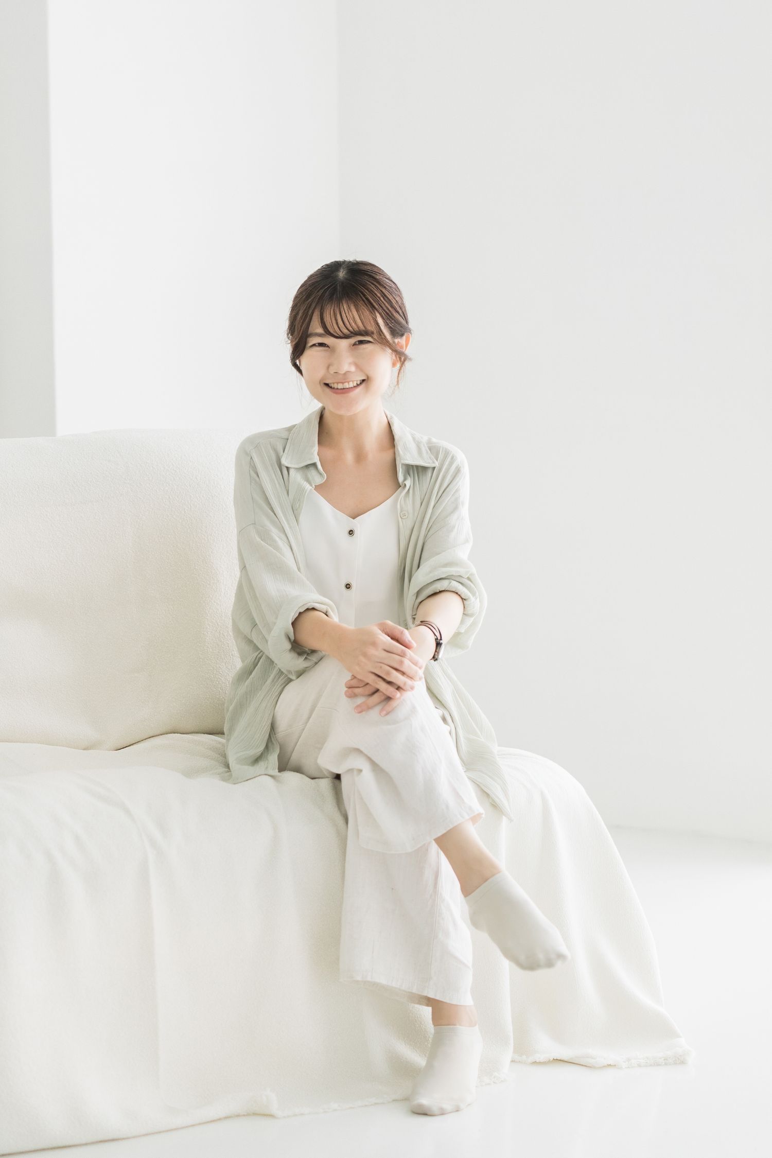 A person in white loungewear sits comfortably on a white couch in a bright, minimalist setting.