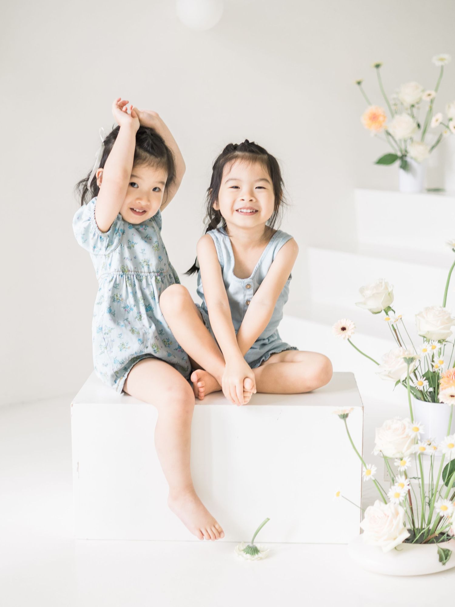 Two children sit together playfully on a white platform with floral decorations.